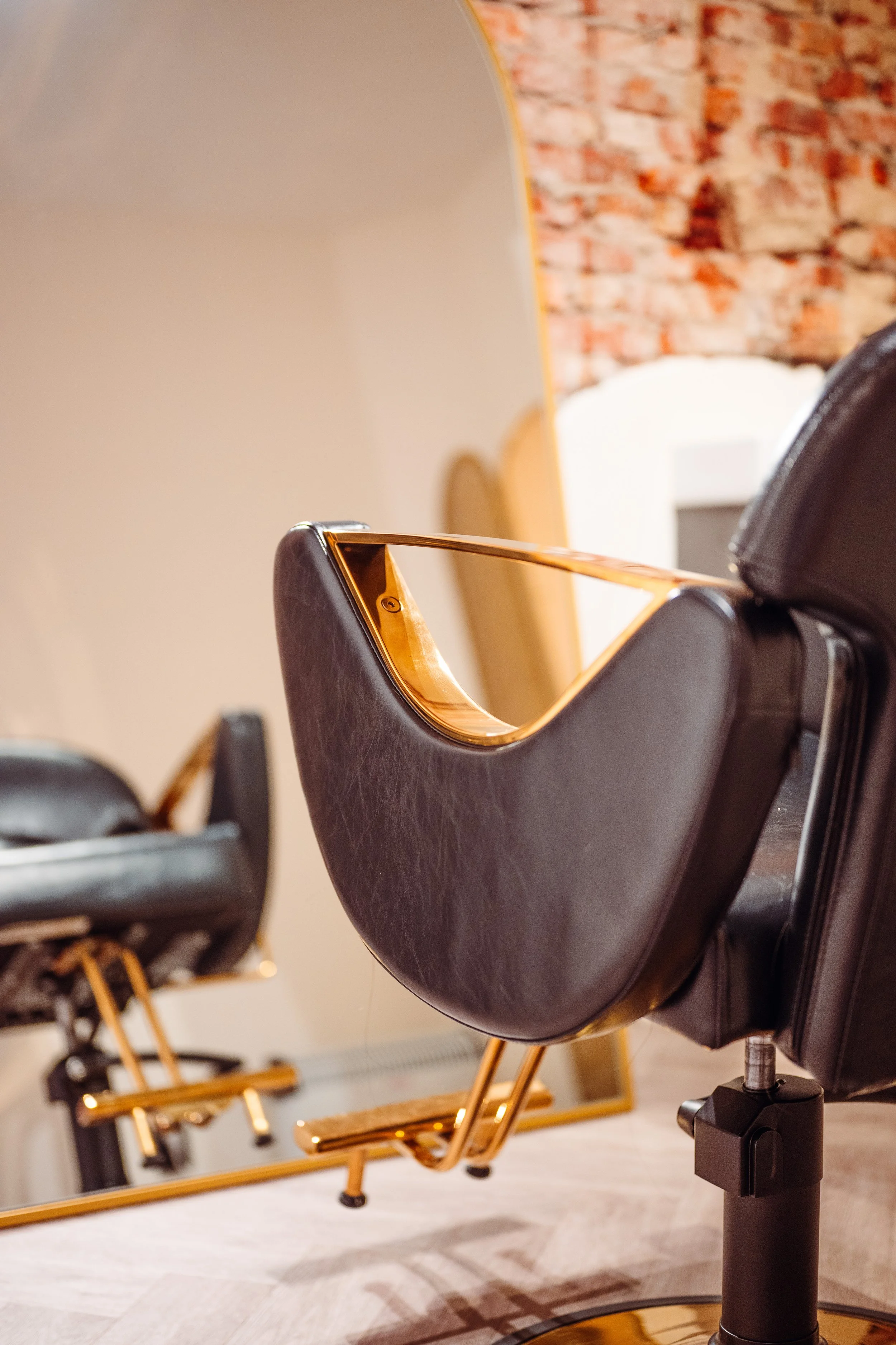 Een dicht bij een draaistoel met zwarte bekleding en gouden frame die zich in een interieur met een beige vloer en een bakstenen muur bevindt.