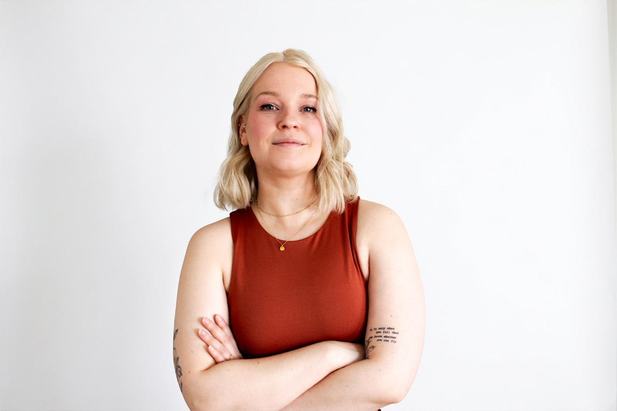 Kaaoskoordinaattori, hymyilee studiossa vaaleaa taustaa vasten ammattimaisessa tyylissä.