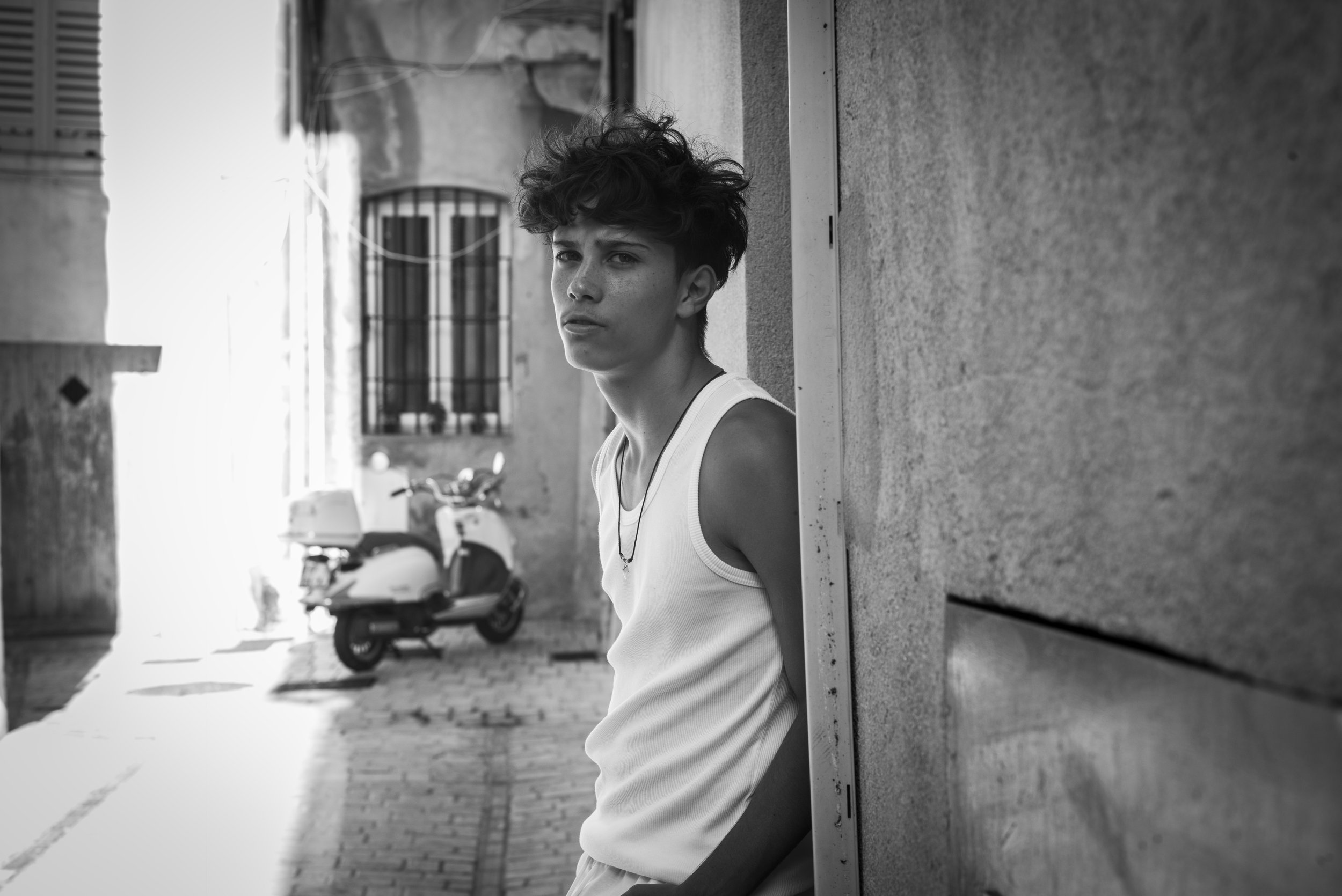 Black-and-white portrait of Sebastien Browning leaning against a doorway, with a scooter in the street behind him.