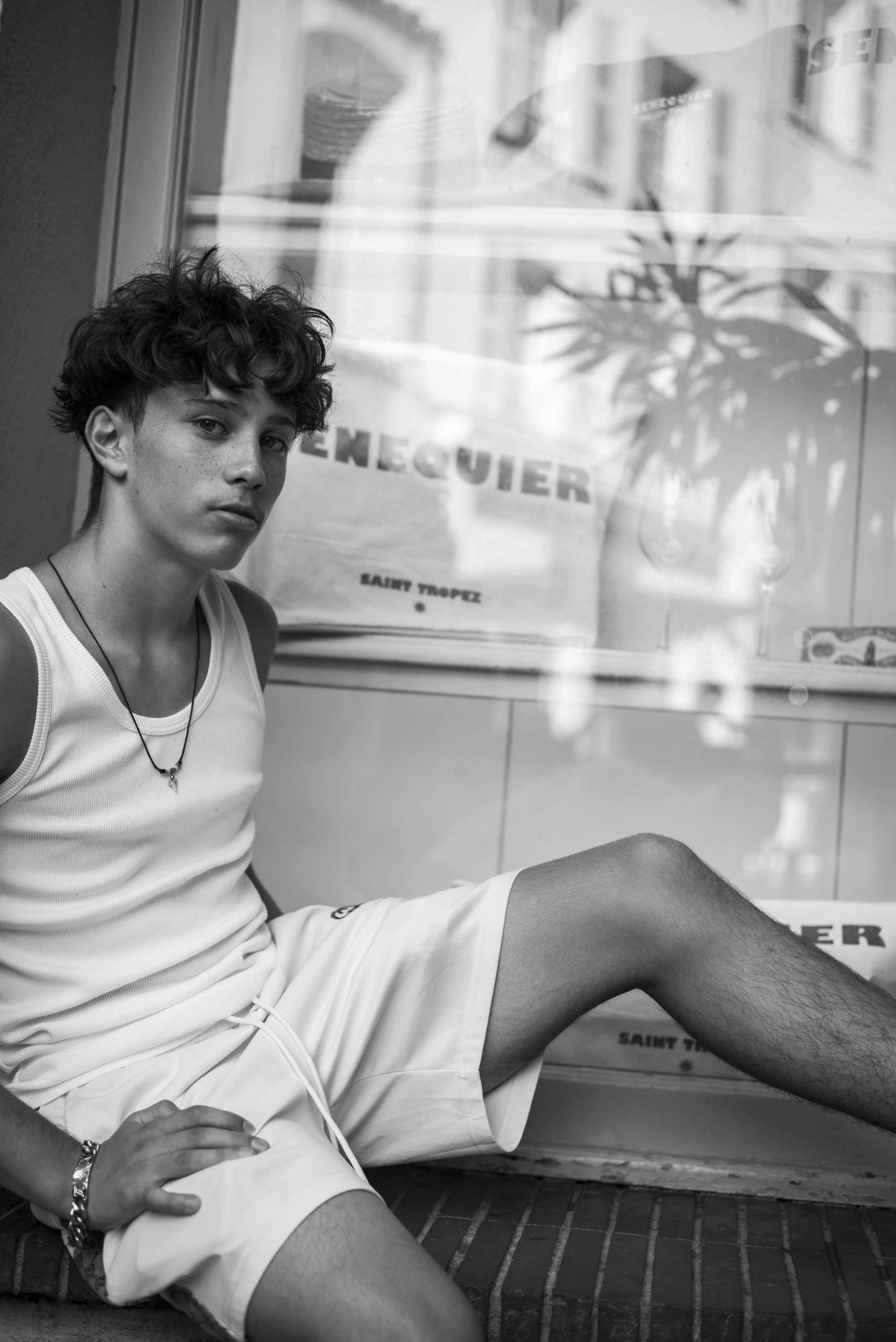 Black-and-white photograph of Sebastien Browning seated beside a shop window, looking towards the camera.