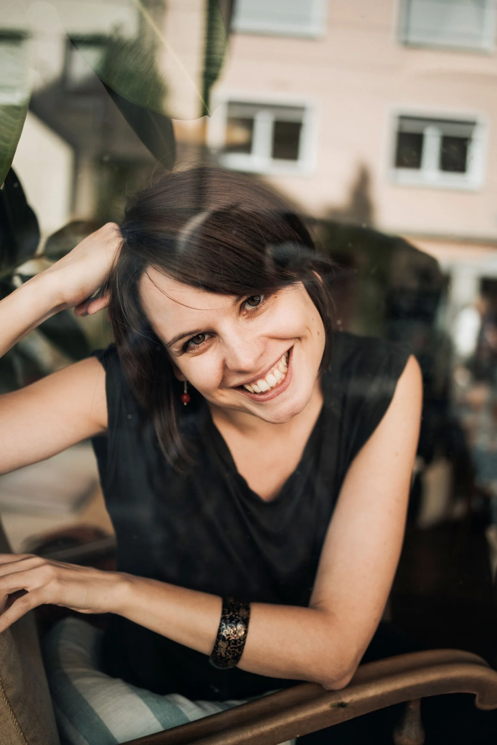 Portrtätfoto von Viola Petsch, lachend hinter einer Glasscheibe eines Cafes sitzend mit Blick in die Kamera
