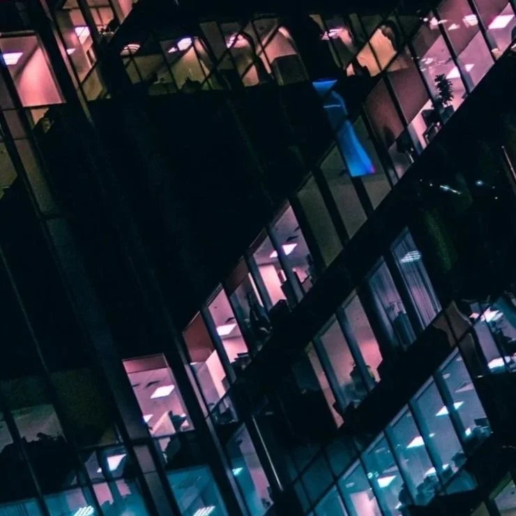 Close-up of a modern glass office building at night, with illuminated interior lights visible through the windows.