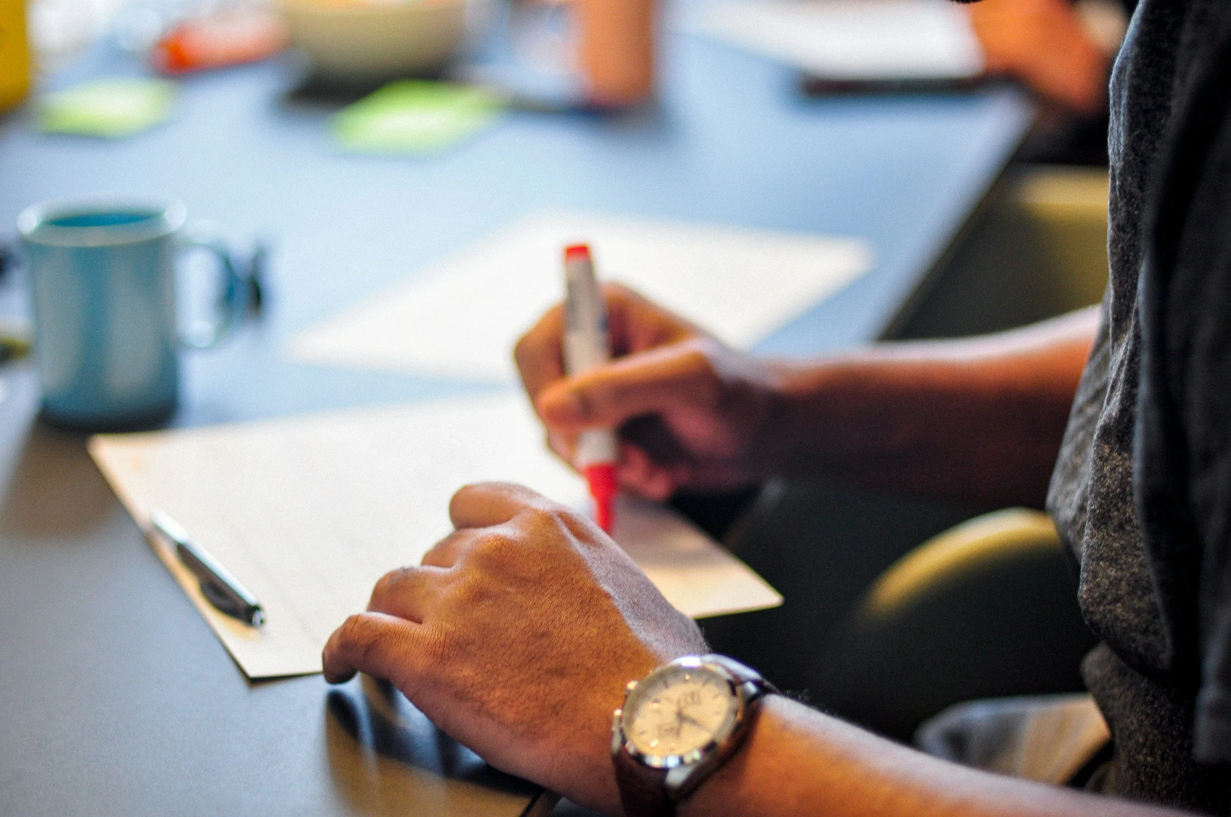 Person holding a whiteboard marker and writing on paper with a blue mug nearby.