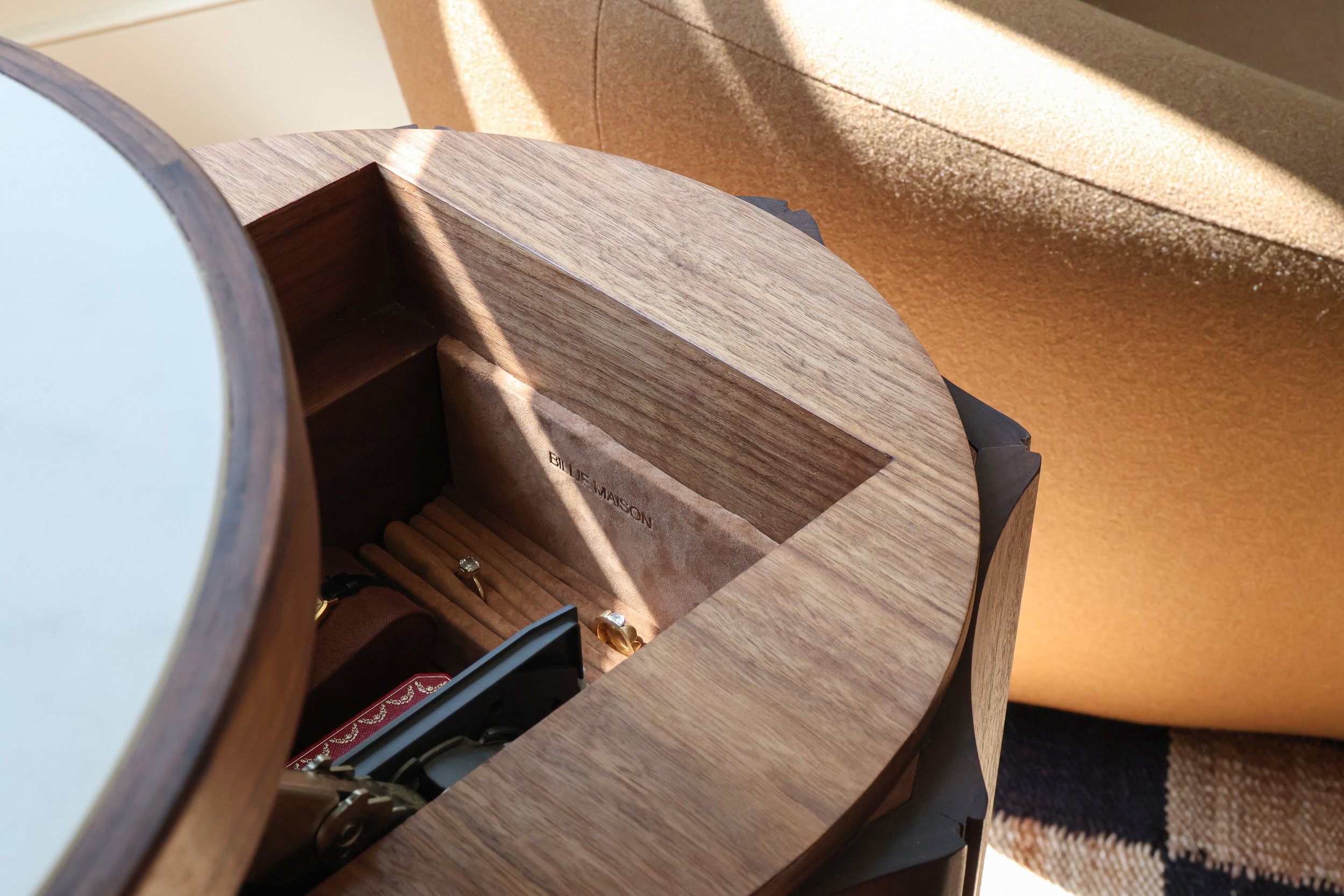 Close-up of a wooden jewelry hidden compartment box, containing rings and jewelry, placed on a wooden surface, with a textured beige background.