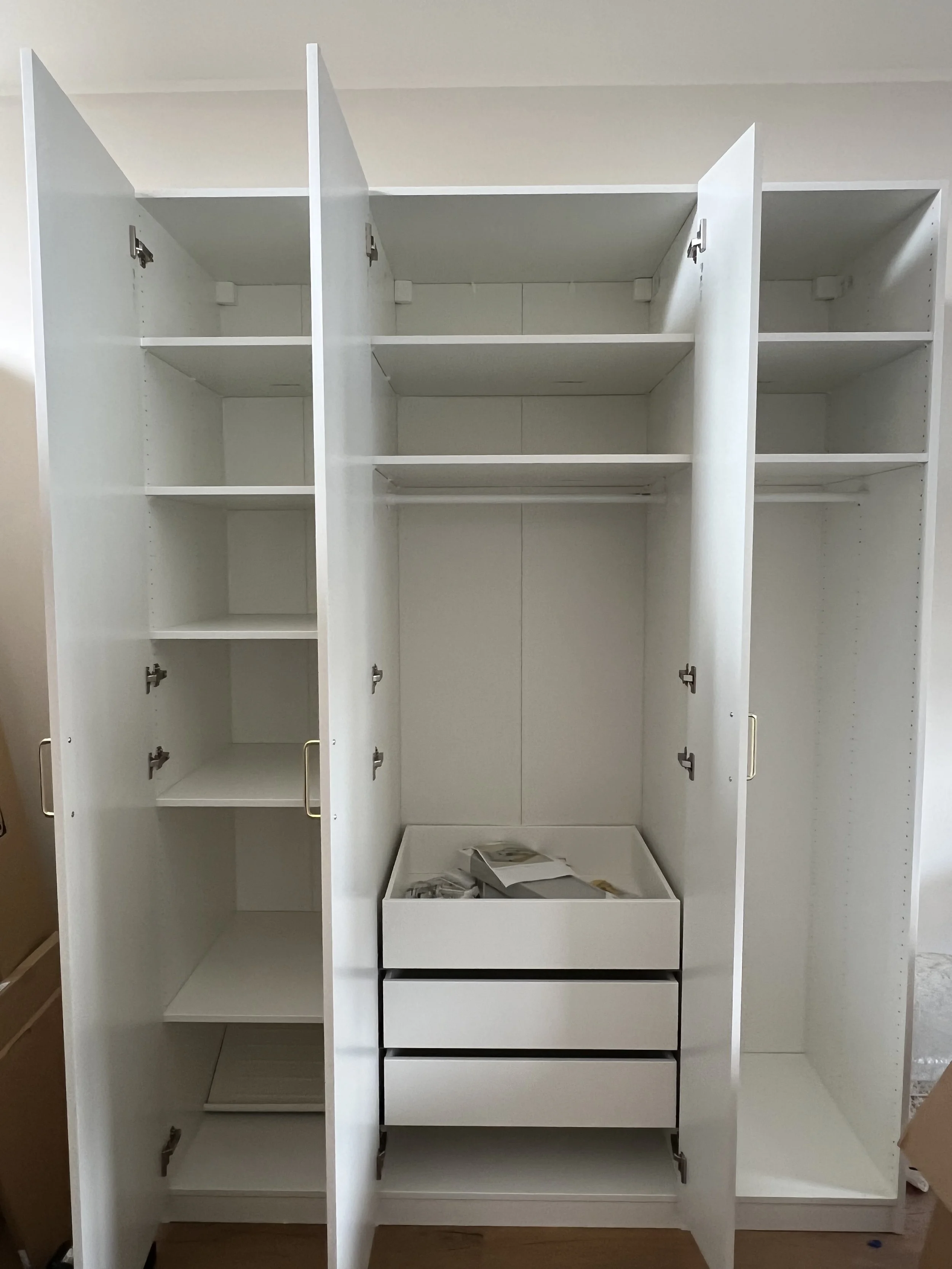Ein weißer Schrank mit offenen Türen, mehreren Fächern und Schubladen, in einem Raum mit Holzboden.