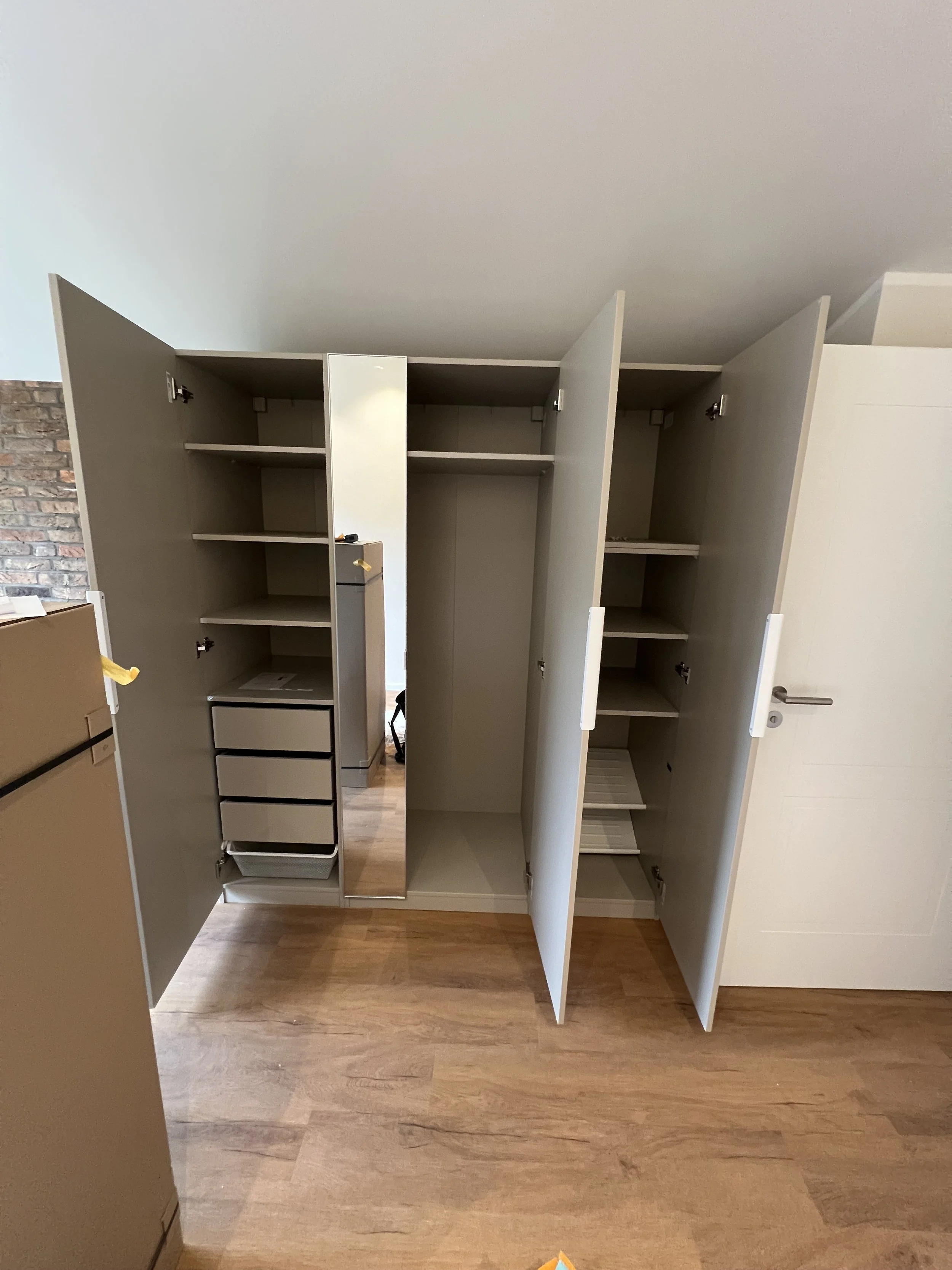 Offene weiß lackierte Schranksysteme mit mehreren Fächern und Schubladen, vor einer Wand im Raum.