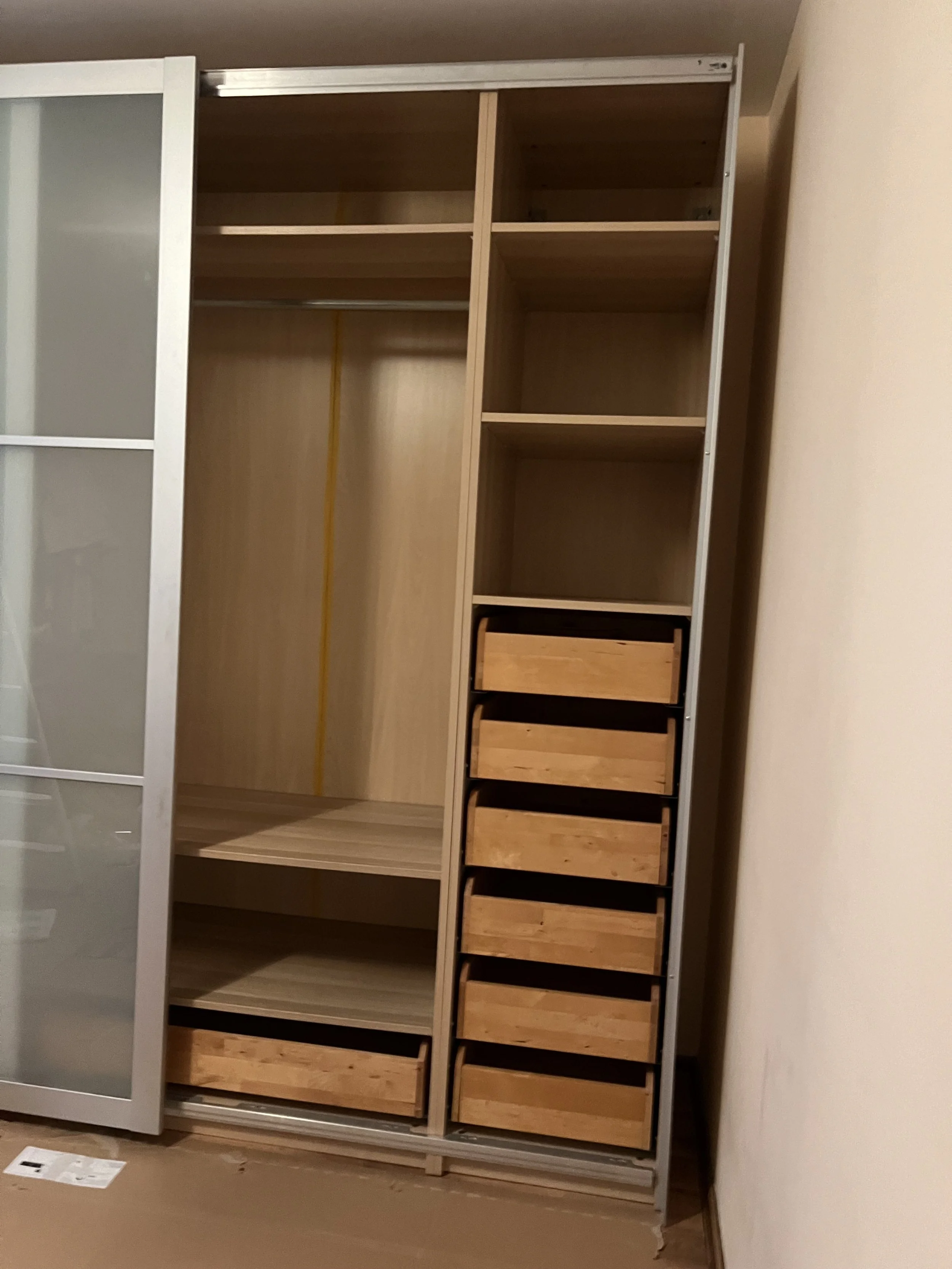 Ein leerer Kleiderschrank mit Holz- und Metallteilen, mehreren Fächern, Schubladen und einer Kleiderstange.