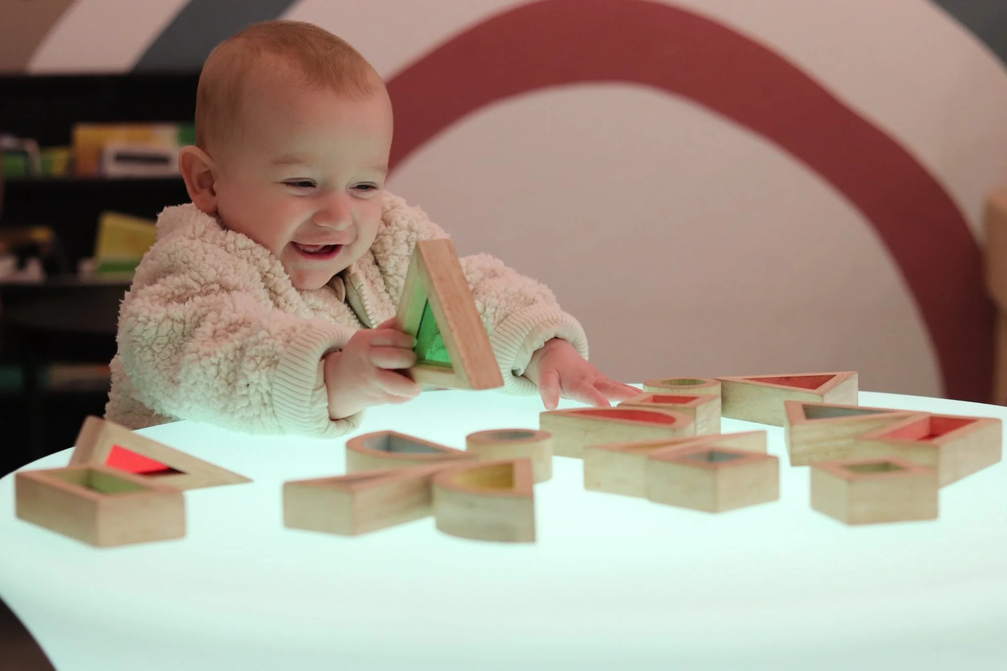 A young child playing with wooden alphabet blocks at a brightly lit table.