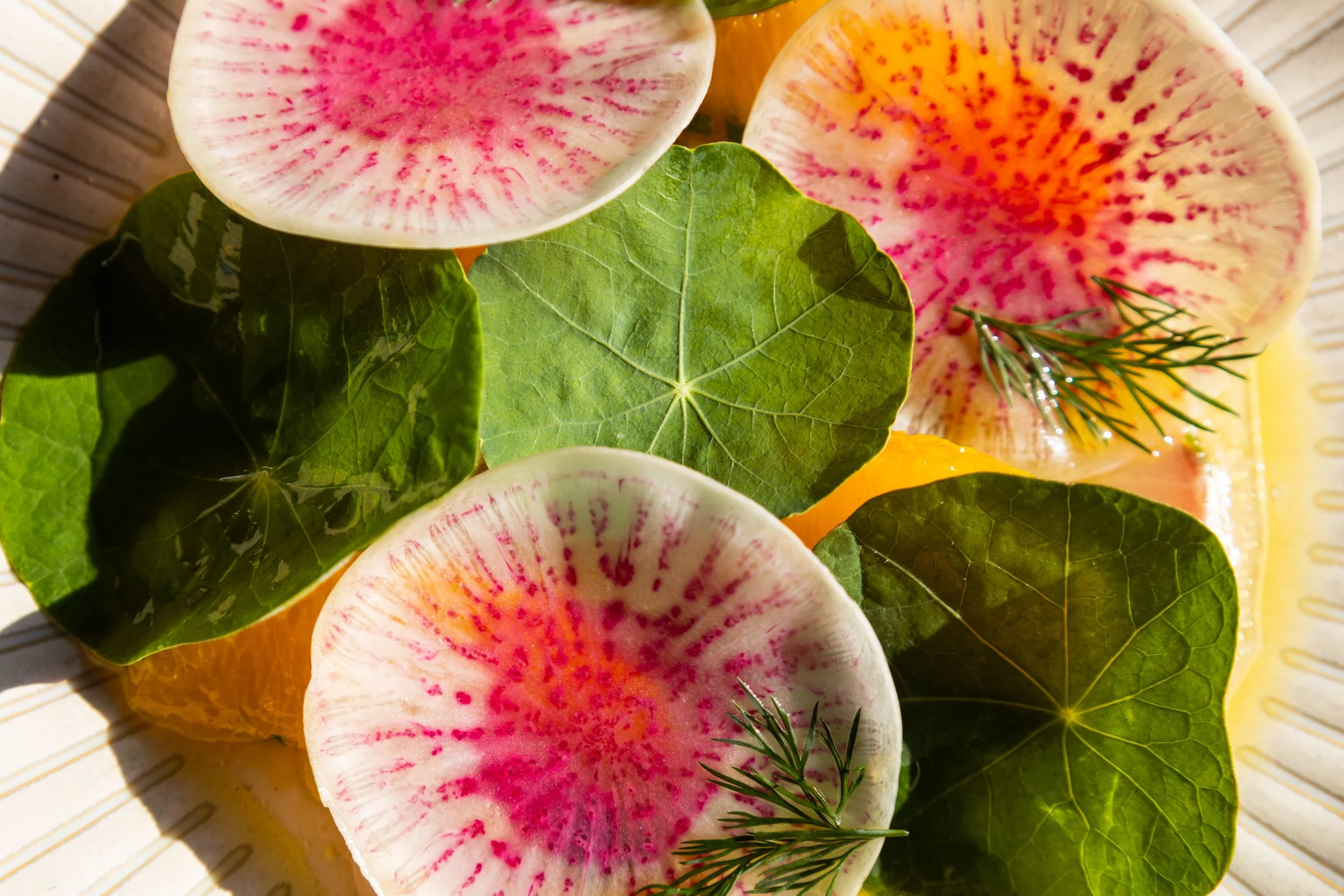 Close-up of colourful food and green leaves on a yellow sauce with a plate in the background.