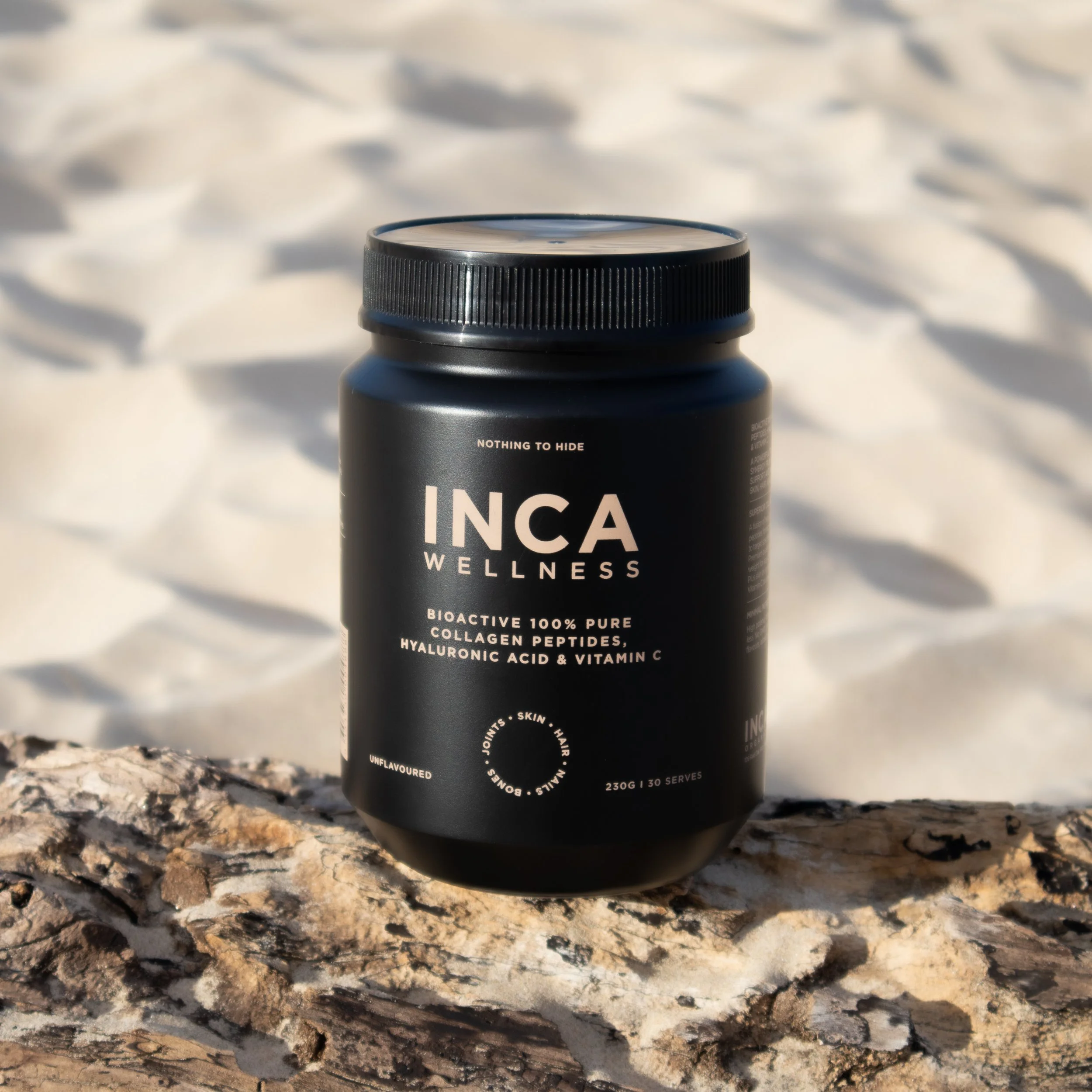 A black bottle labeled 'INC' with wellness and collagen topics on a textured rock surface outdoors in bright sunlight.
