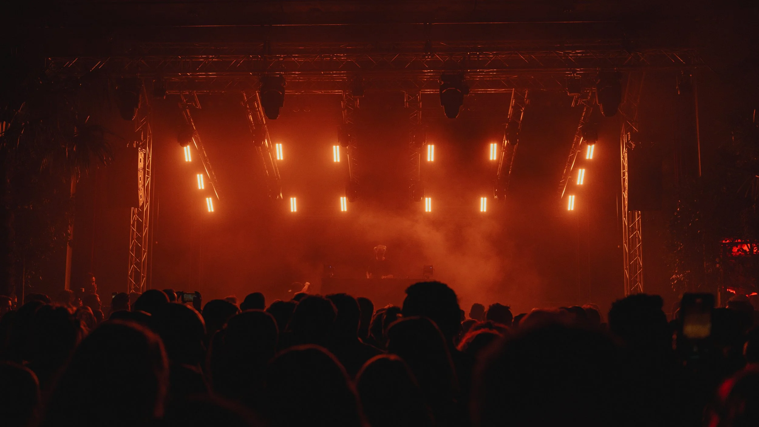 Bühne mit roten Lichtern bei einem nächtlichen Musikfestival, Menschen im Publikum sind silhouettenhaft zu sehen.