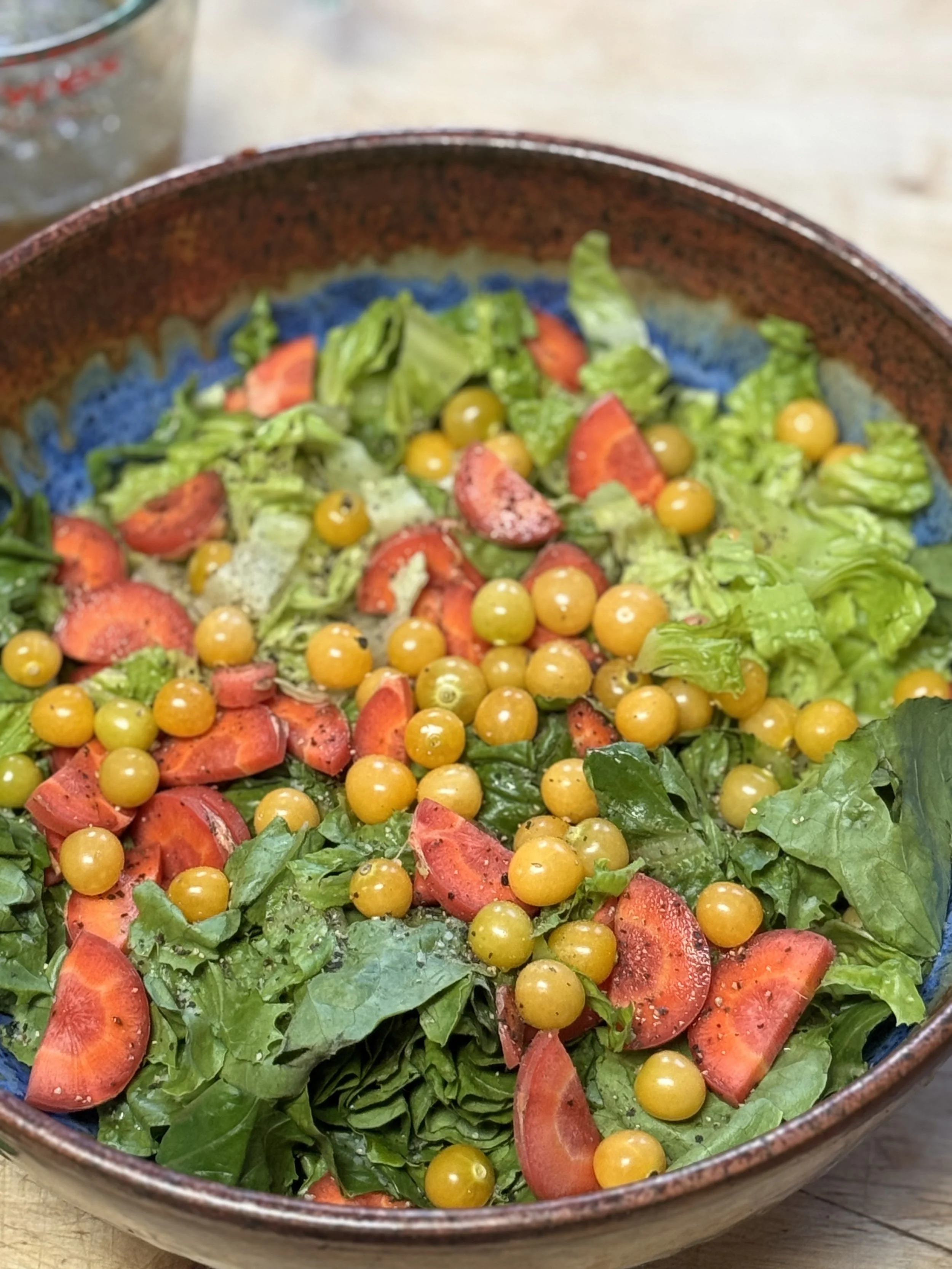 Fresh salad with spinach, sliced strawberries, and yellow berries in a ceramic bowl.