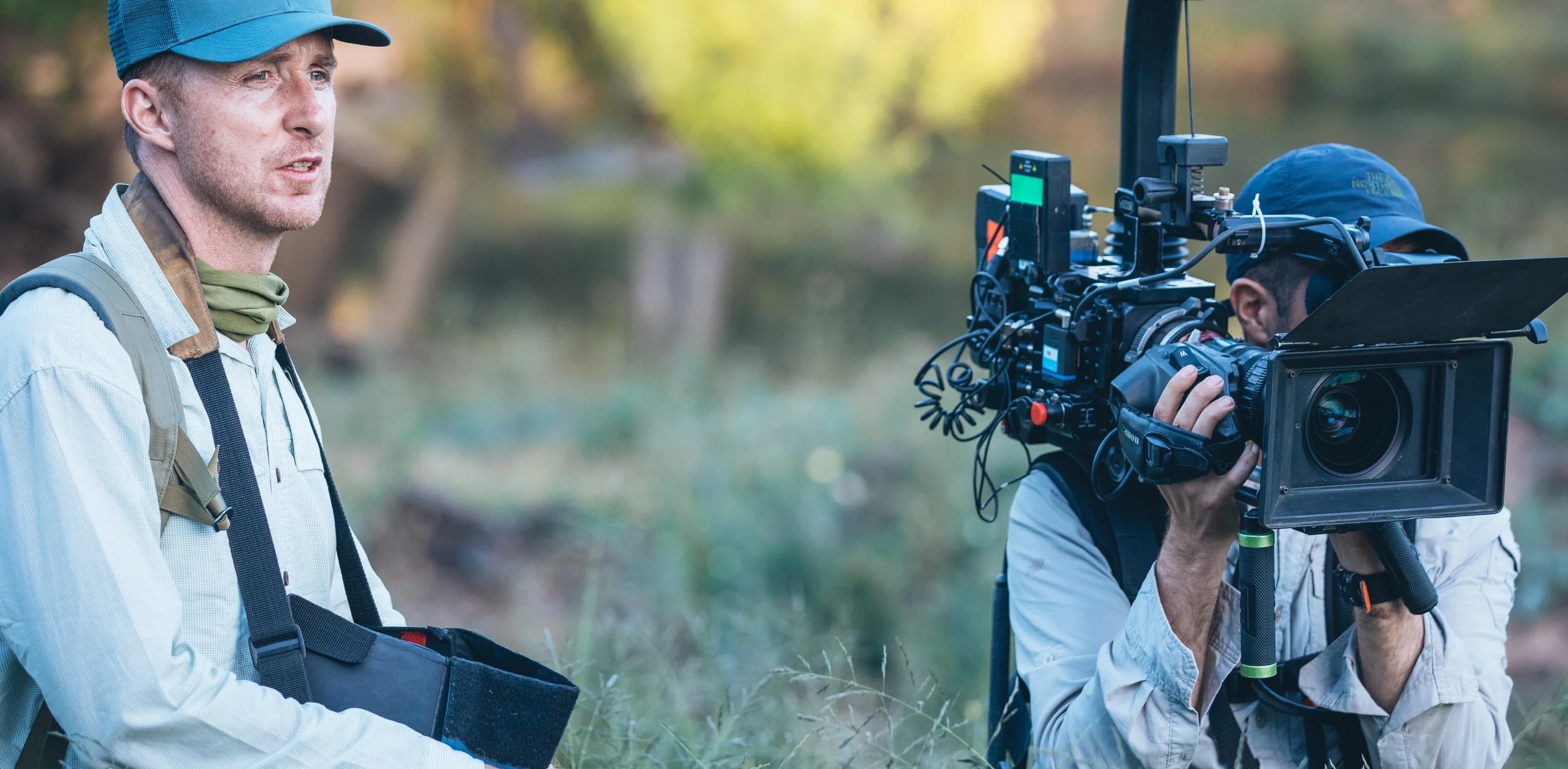 Filmmaker Jody Bourton on set directing a professional video camera outdoors on a grassy area with blurred background.
