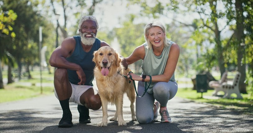 An older man and woman with a golden retriever dog in a park, smiling and posing for a photo.