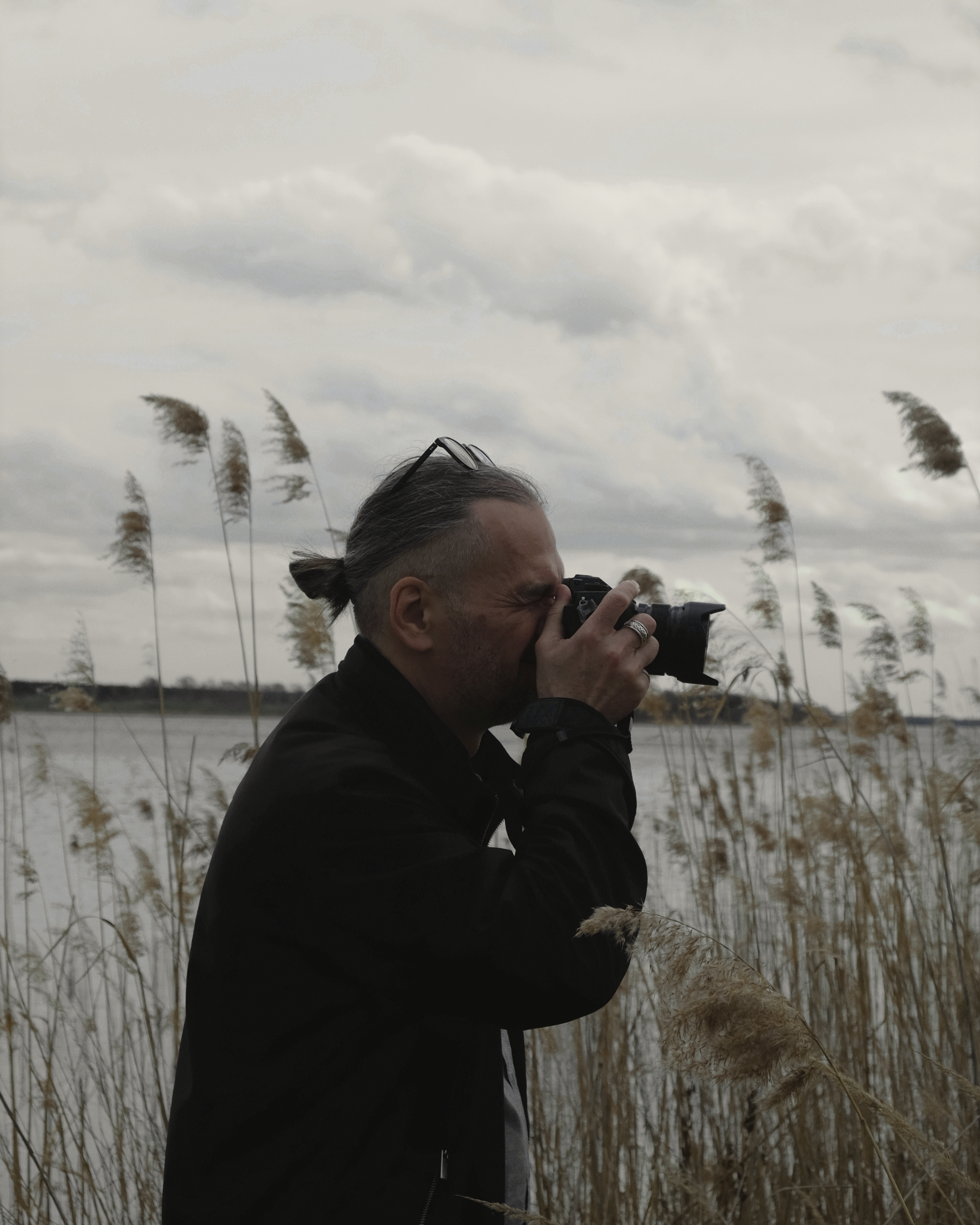 Karsten Löperick fotografiert mit einer Kamera am Wasser zwischen Schilf