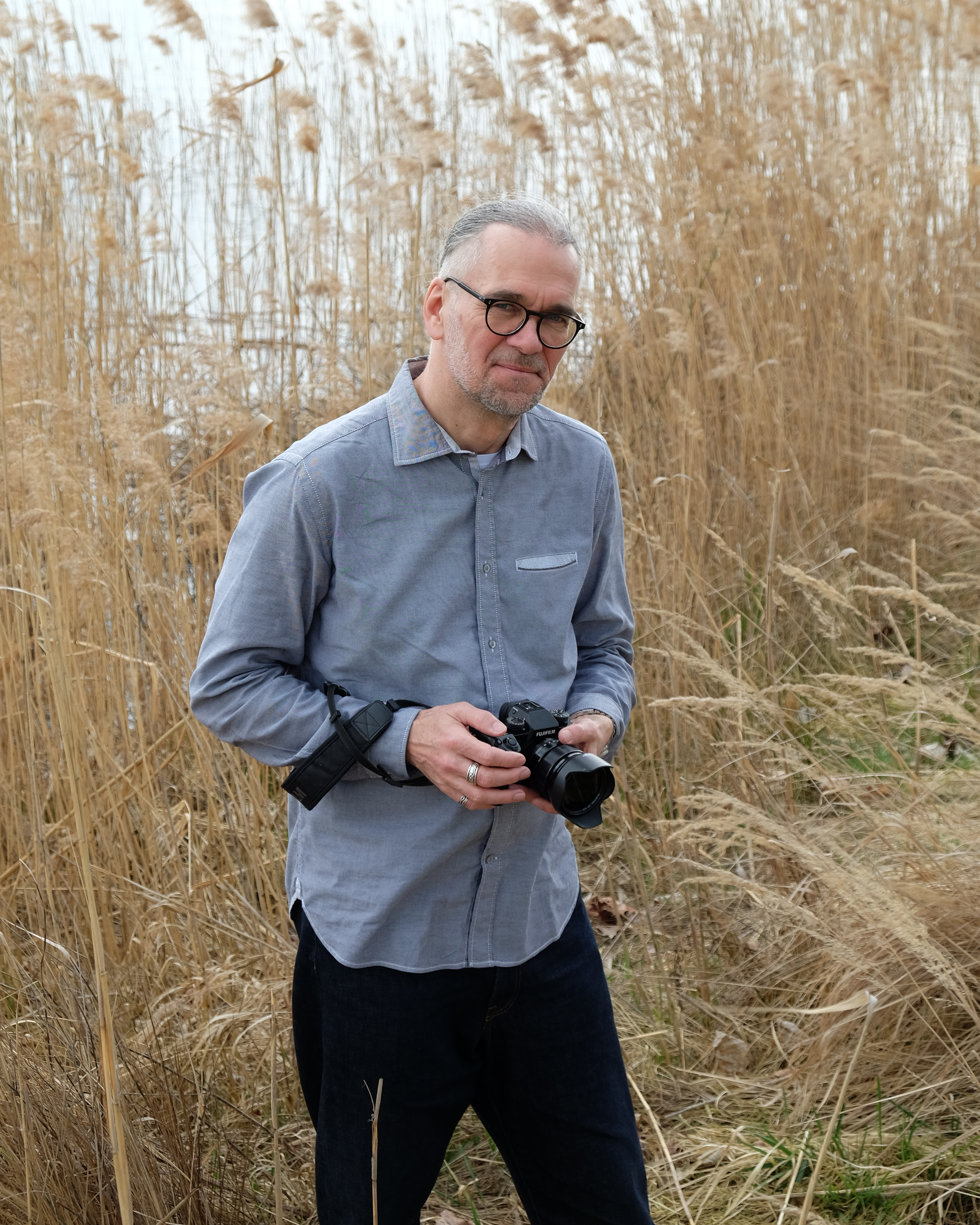 Fotograf Karsten Löperick mit Kamera vor beigem Naturhintergrund