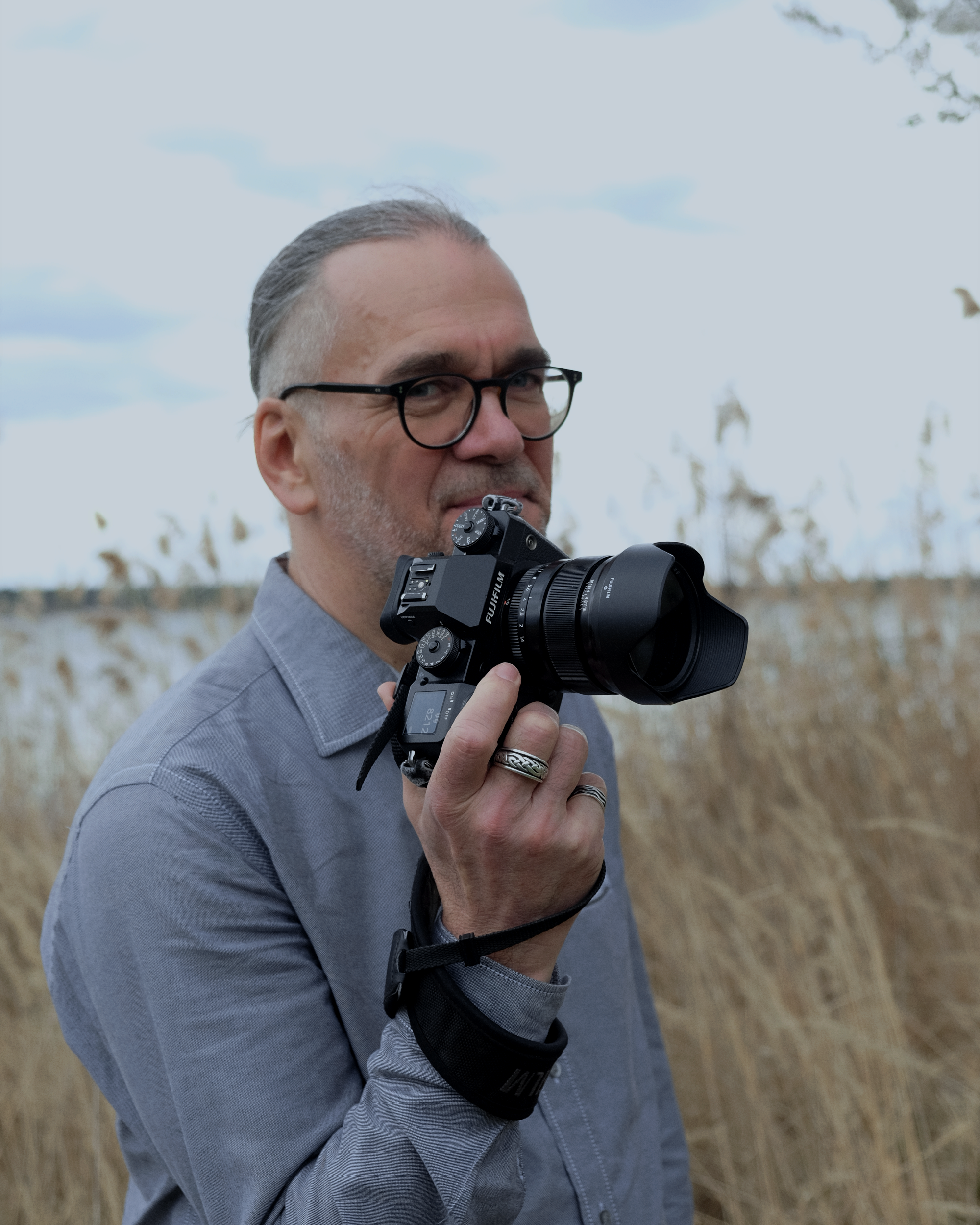 Karsten Löperick, Fotograf und Gründer von Ernst.Haft, mit Kamera in einer natürlichen Uferlandschaft