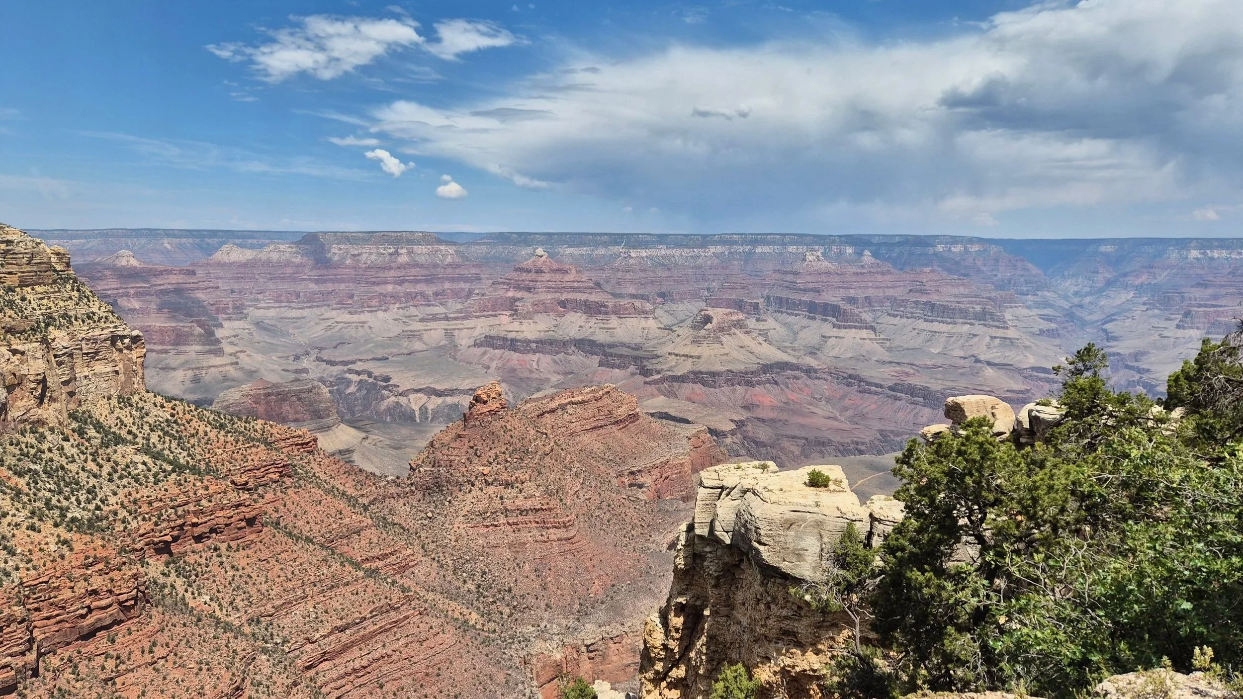 The image shows the Grand Canyon with layered rock formations, some green vegetation, and a partly cloudy sky.