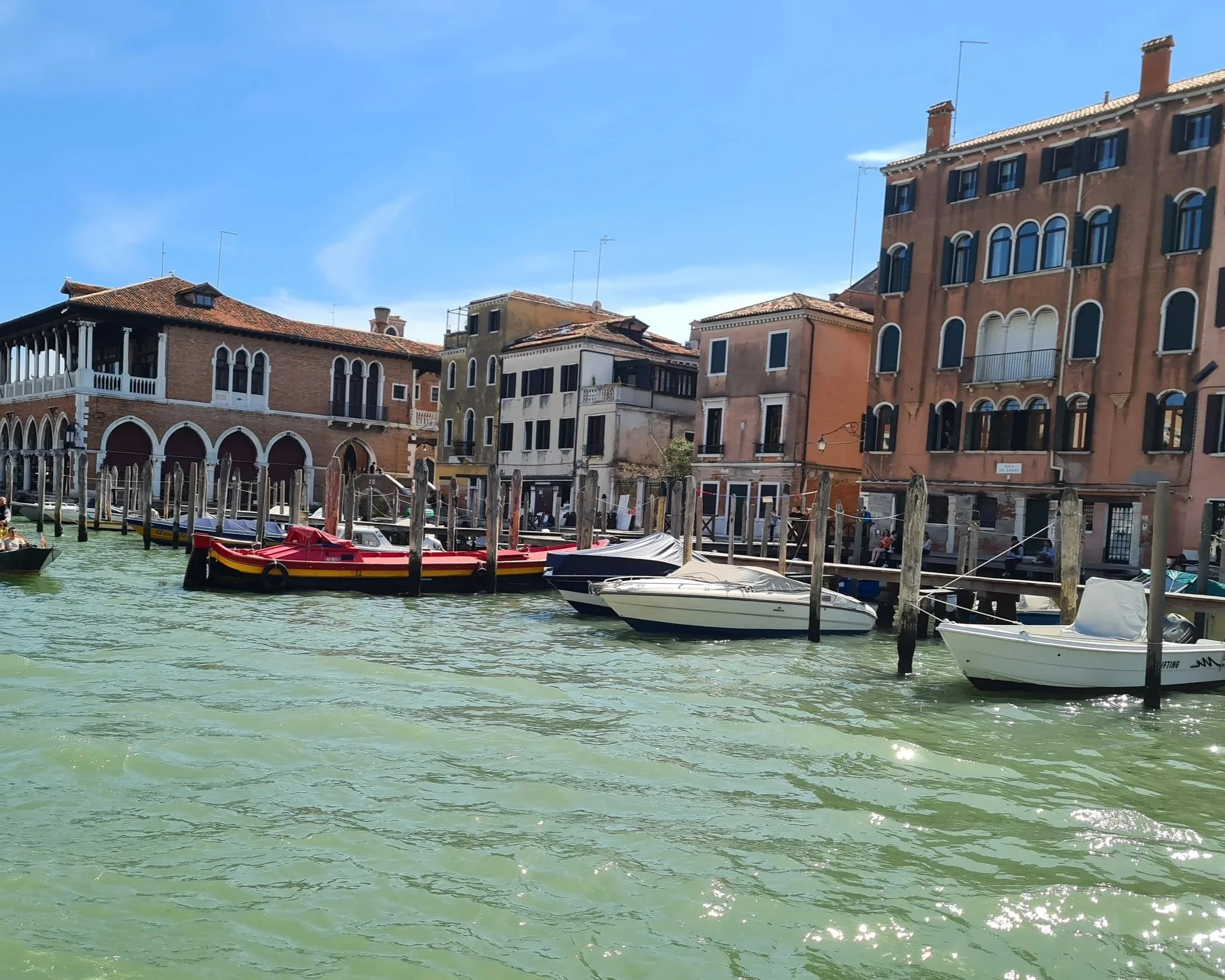 View of historic buildings along a canal with boats docked and a blue sky overhead.