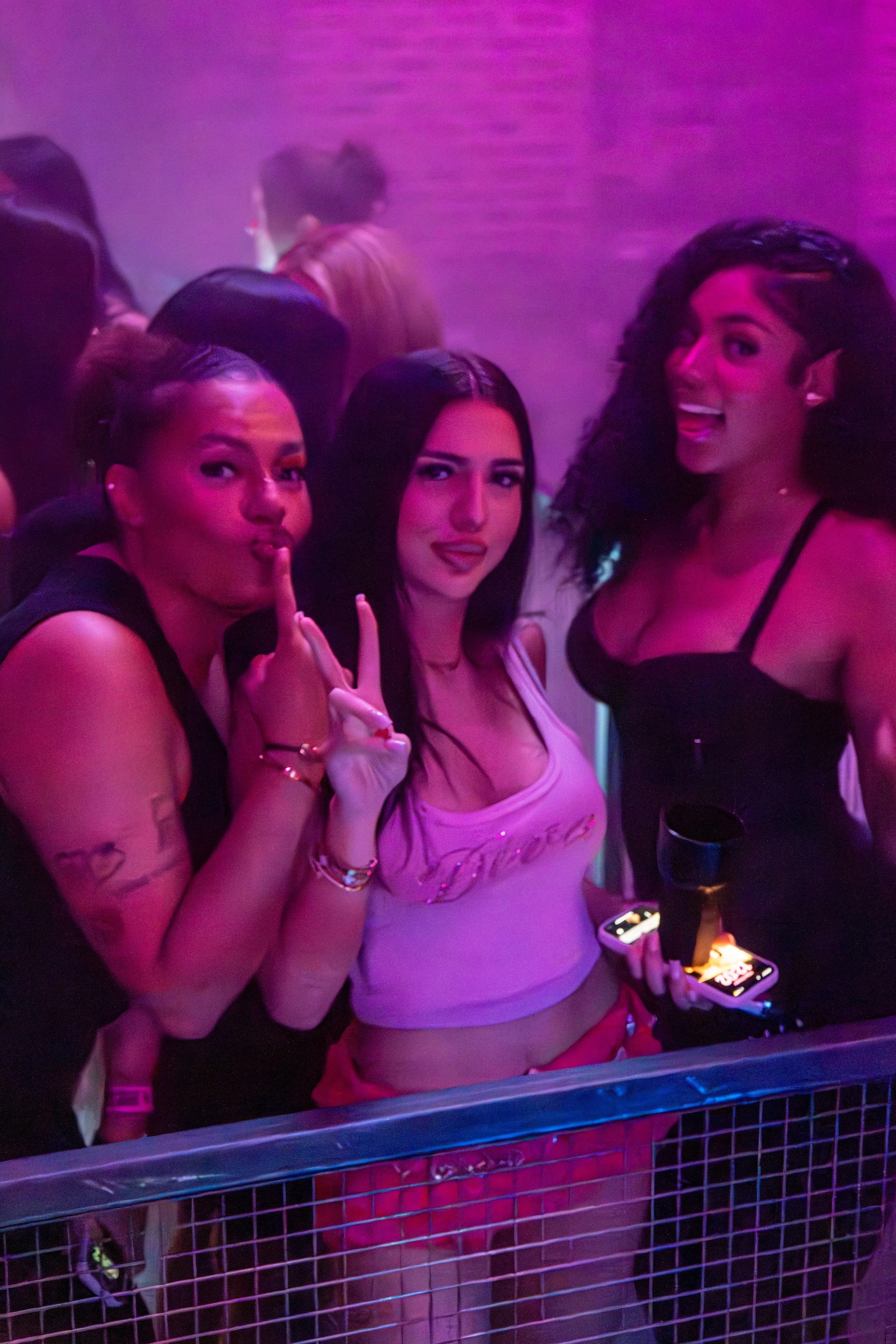Three women at a party with pink and purple lighting, posing for the camera.