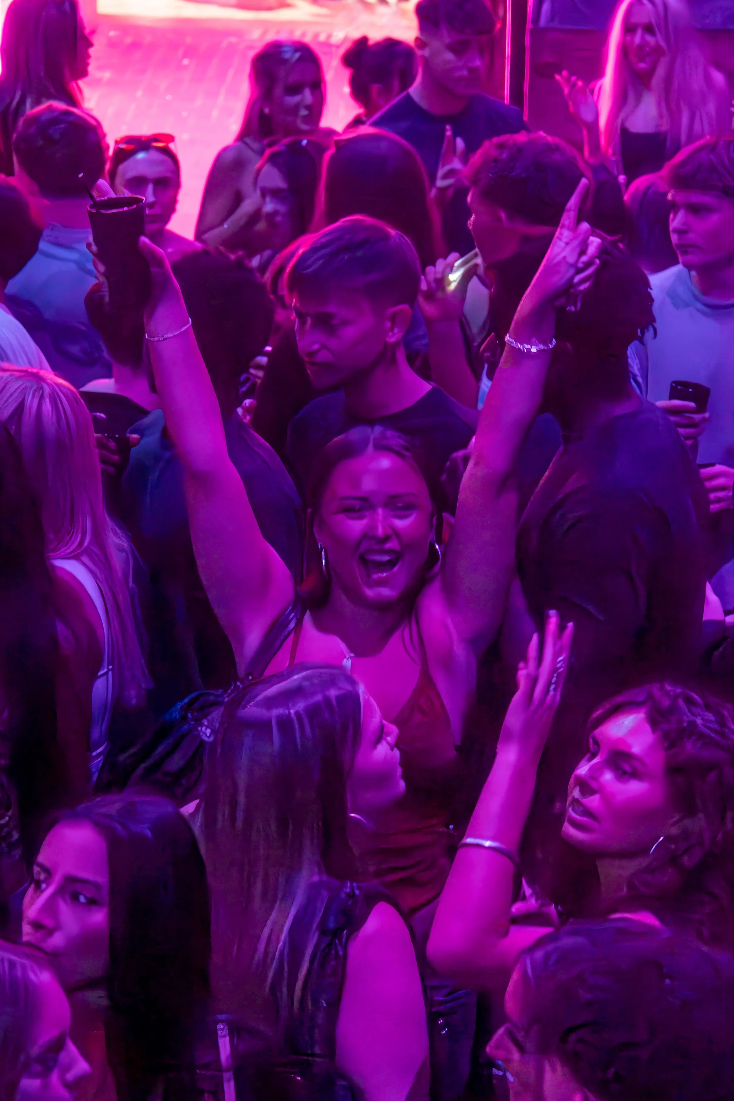 A group of young people dancing and having fun at a party with purple and pink lighting.