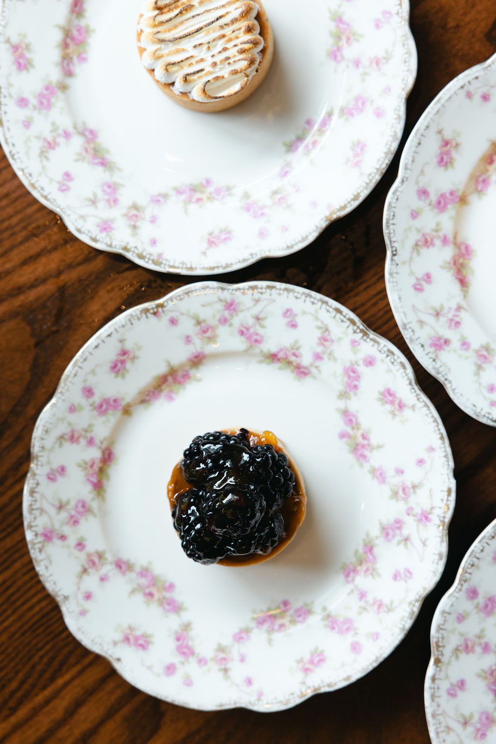 Two dessert pastries on floral china plates, one with blackberries, the other with a toasted lemon meringue topping.