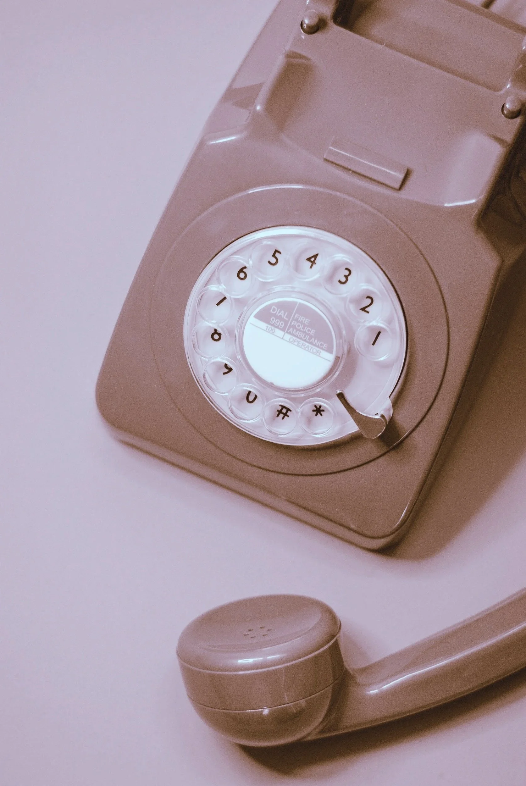 A beige rotary telephone with a circular dial pad resting on a light-colored surface.