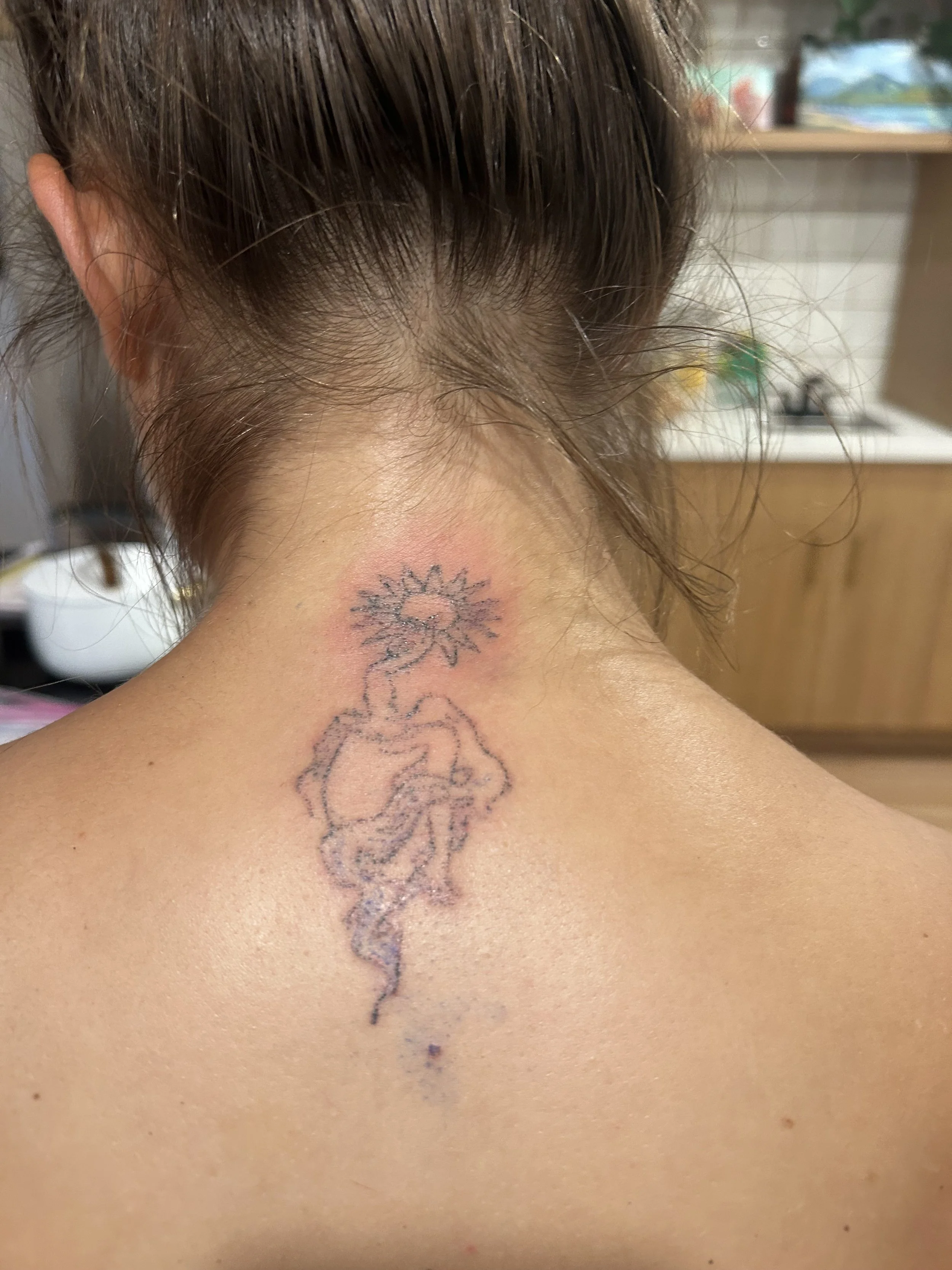 Close-up of the back of a person's neck with a tattoo of a stylized flower and other decorative elements.