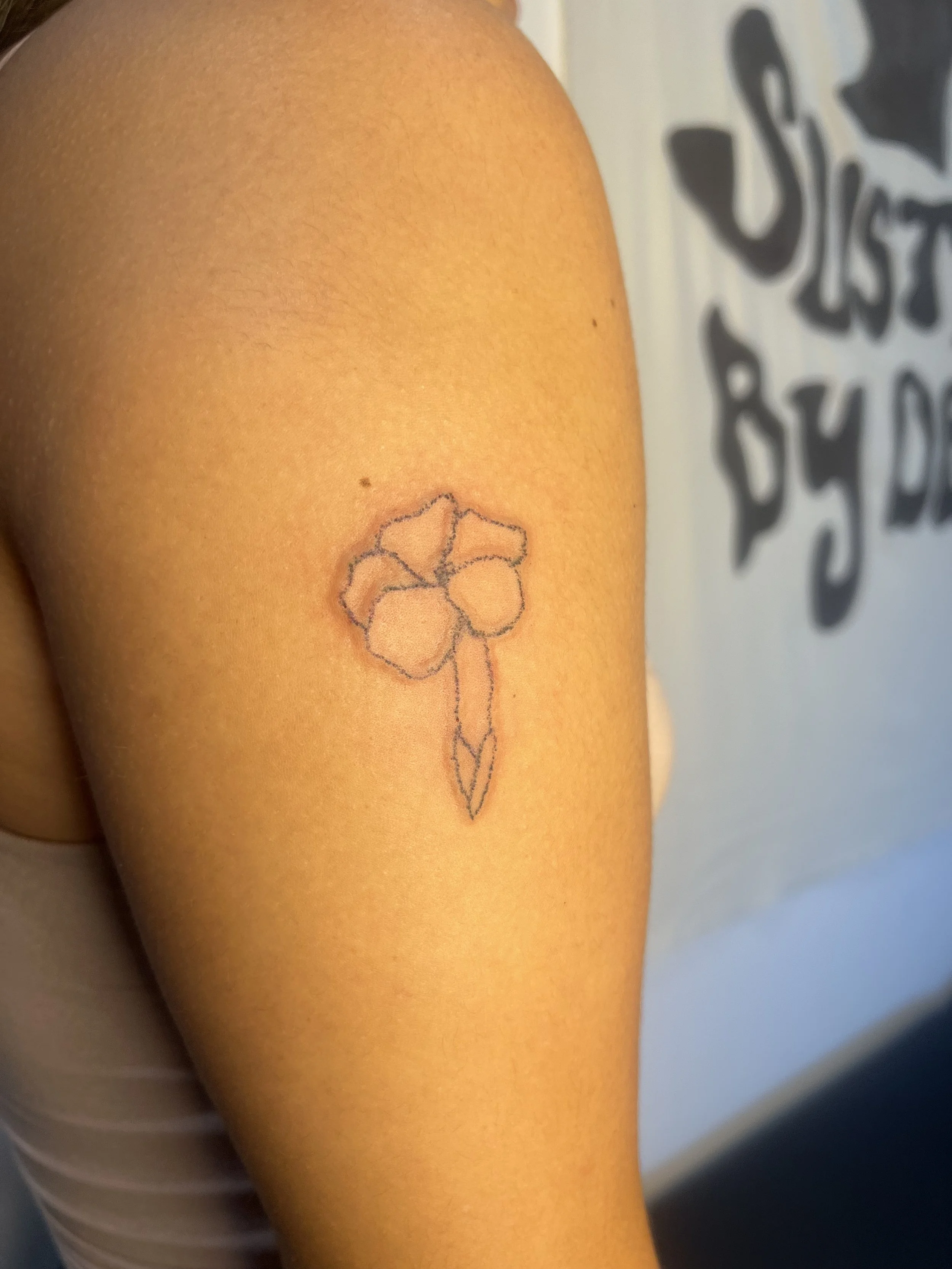 A close-up of a person's shoulder with a small flower tattoo on the upper arm.