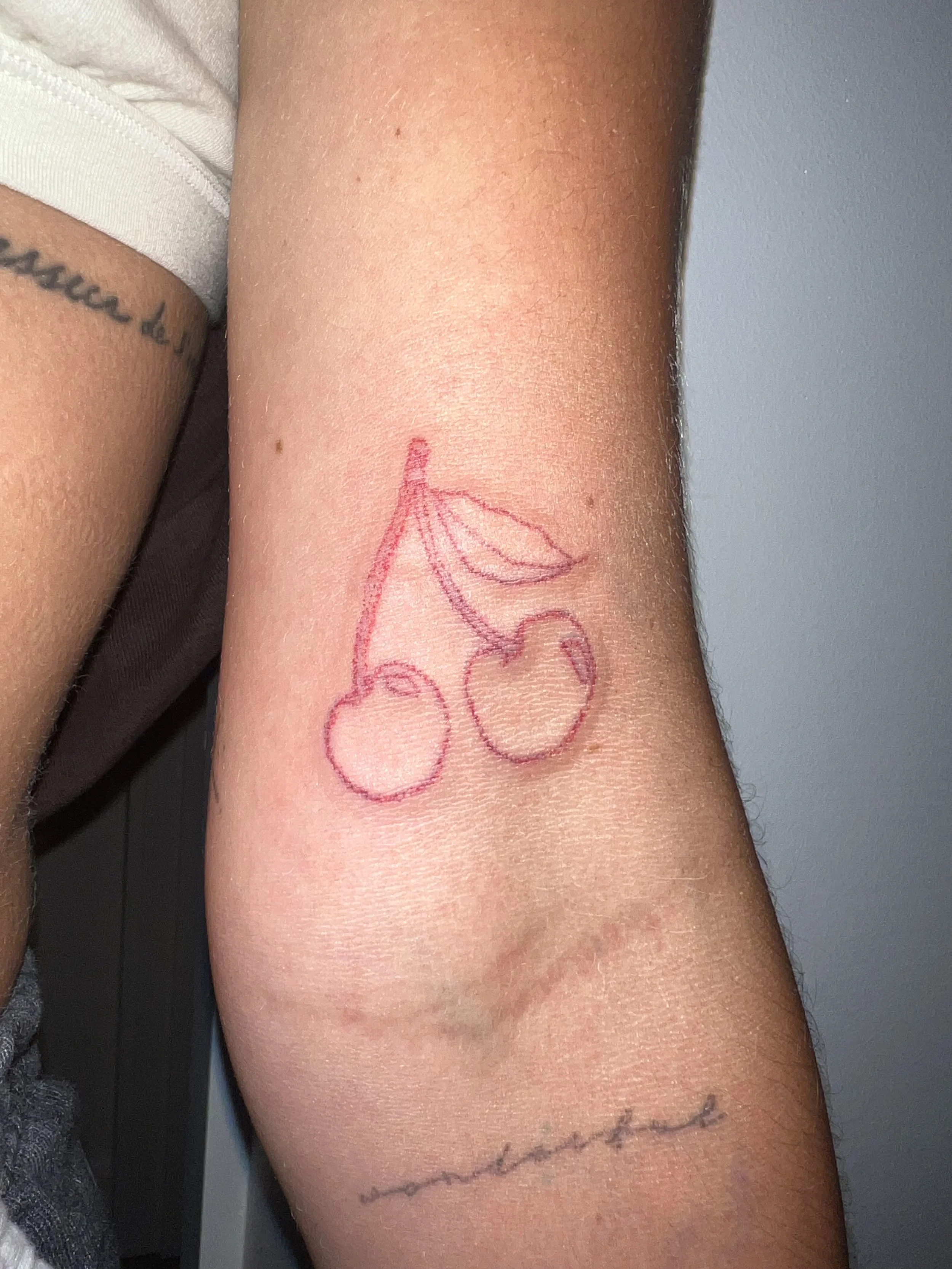 Close-up of a person's arm with two tattoos: one is a cursive word on the wrist, and the other is a red outline of a cartoon elephant with three balloons.