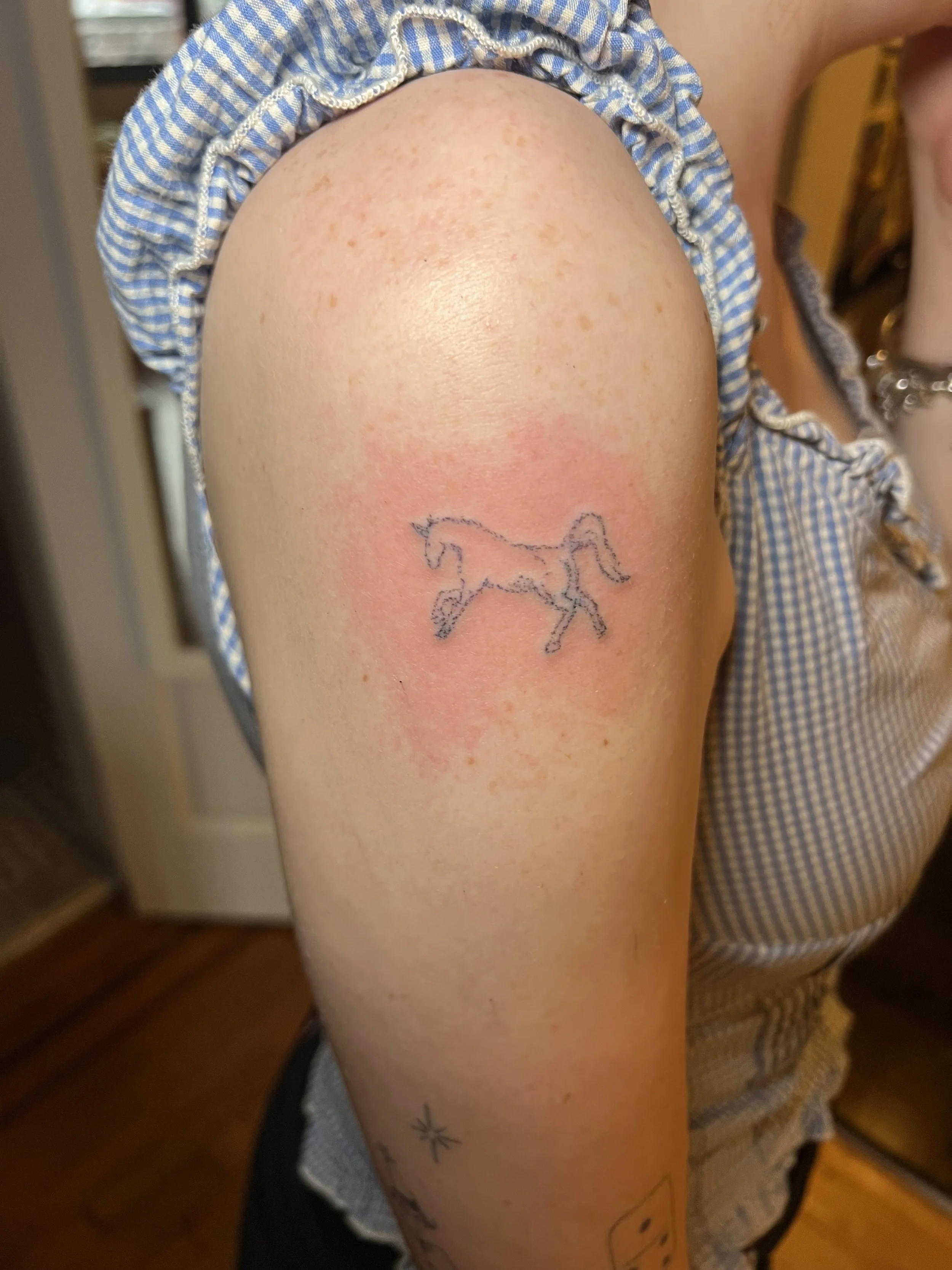 Close-up of a person's upper arm showing a tattoo of a horse and some small stars, with visible redness around the tattoo.