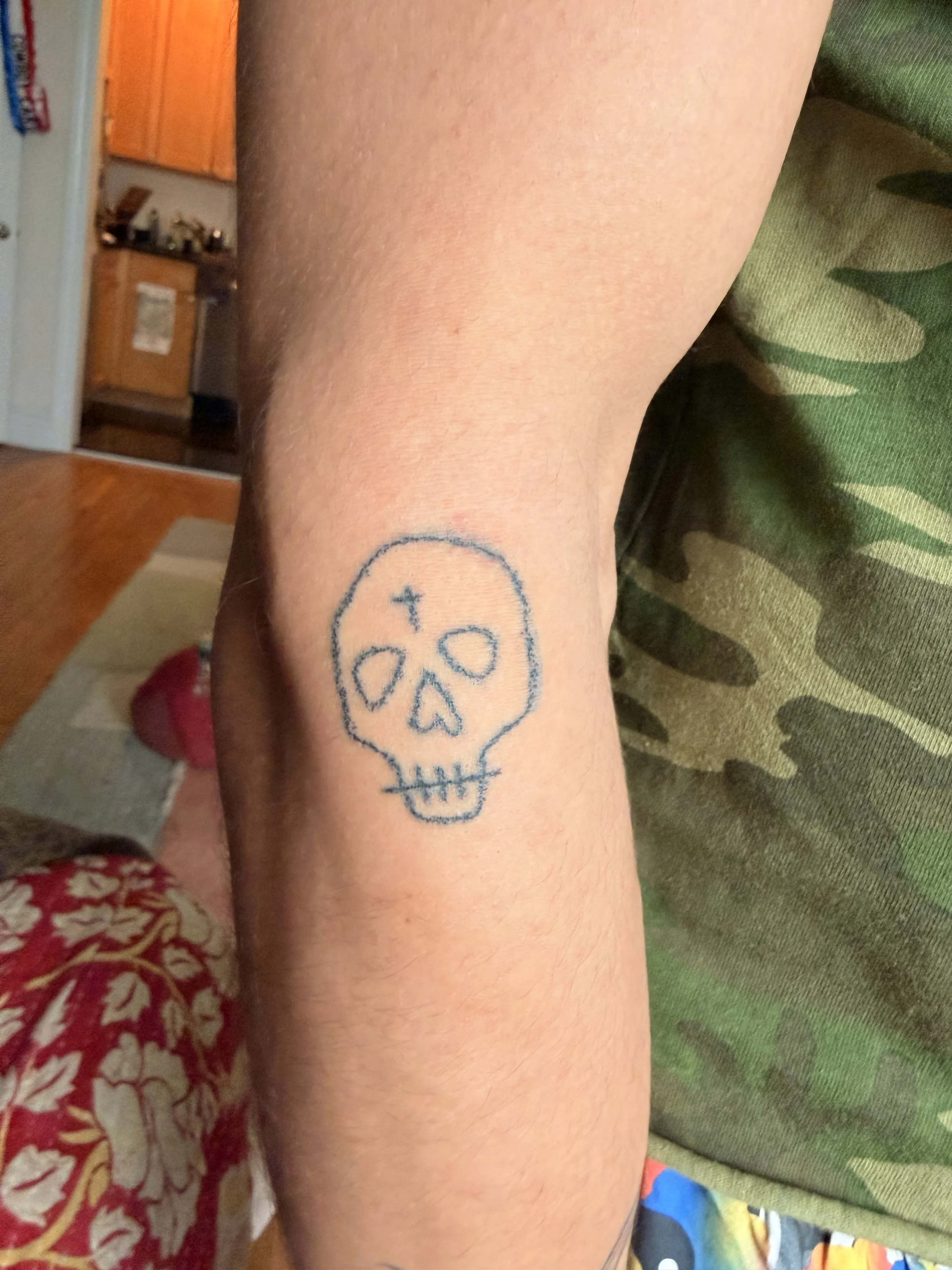 A person's arm with a tattoo of a smiling skull with starry eyes.