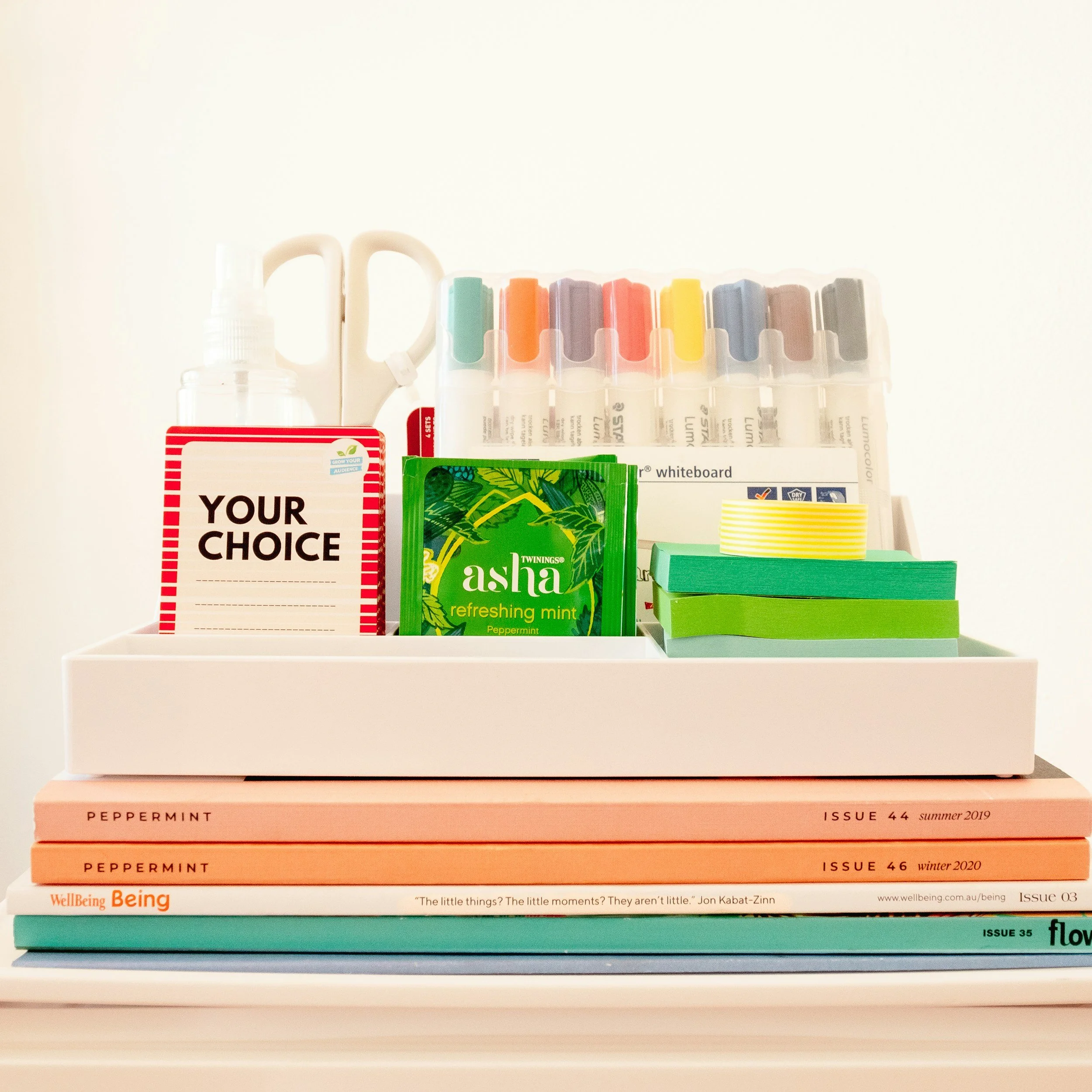 Stacked magazines with the top magazine labeled "YOUR CHOICE" and colorfully arranged pills or swatches on top. Each magazine has a different issue number and date. The magazines are placed on a white surface with a plain background.
