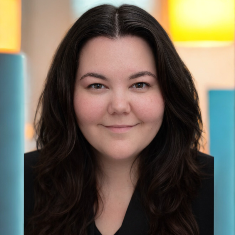 A young woman with long dark hair smiling at the camera, in an indoor setting with soft, colorful lighting.
