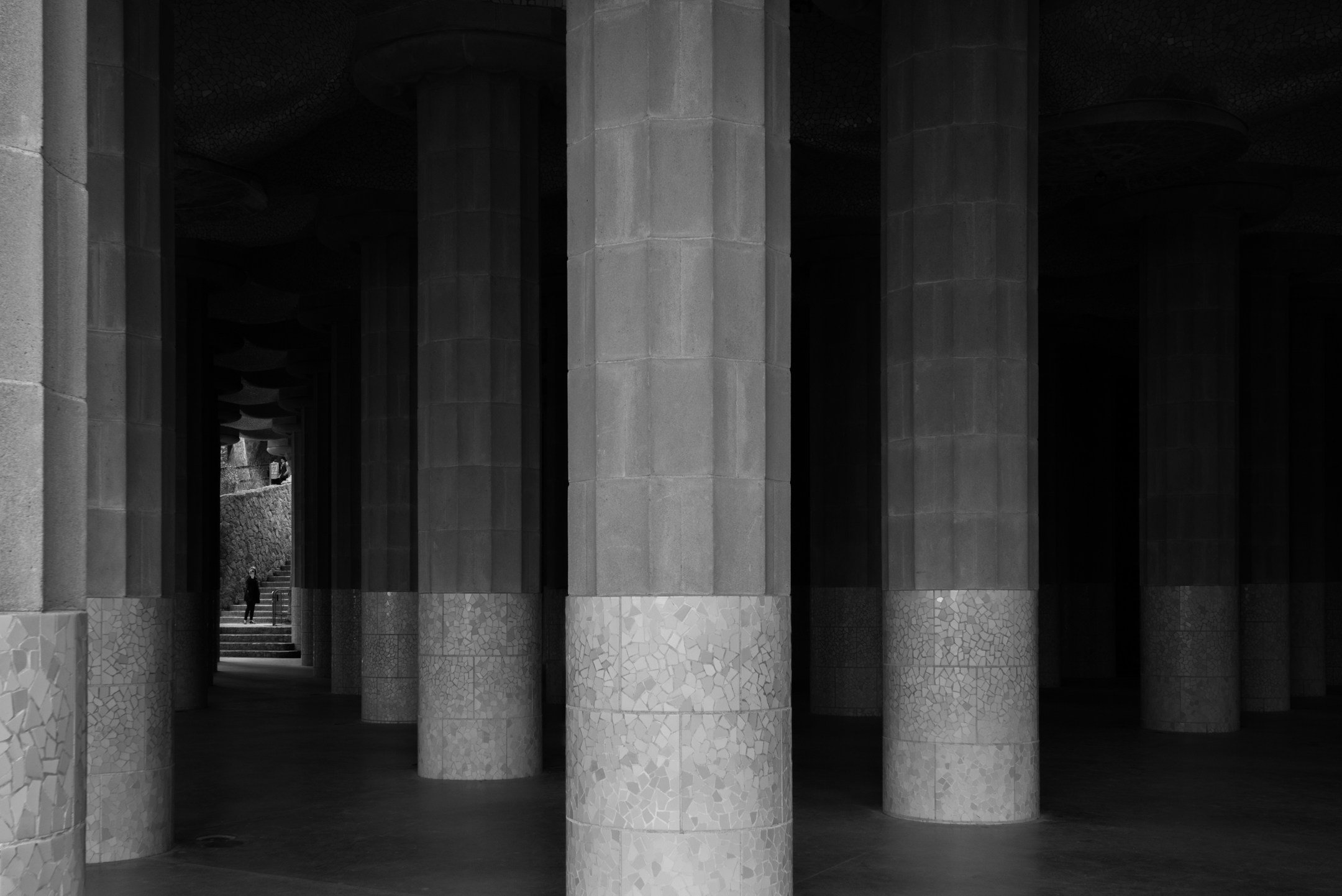 A series of large stone columns forming a covered walkway with stairs and a person in the distance.