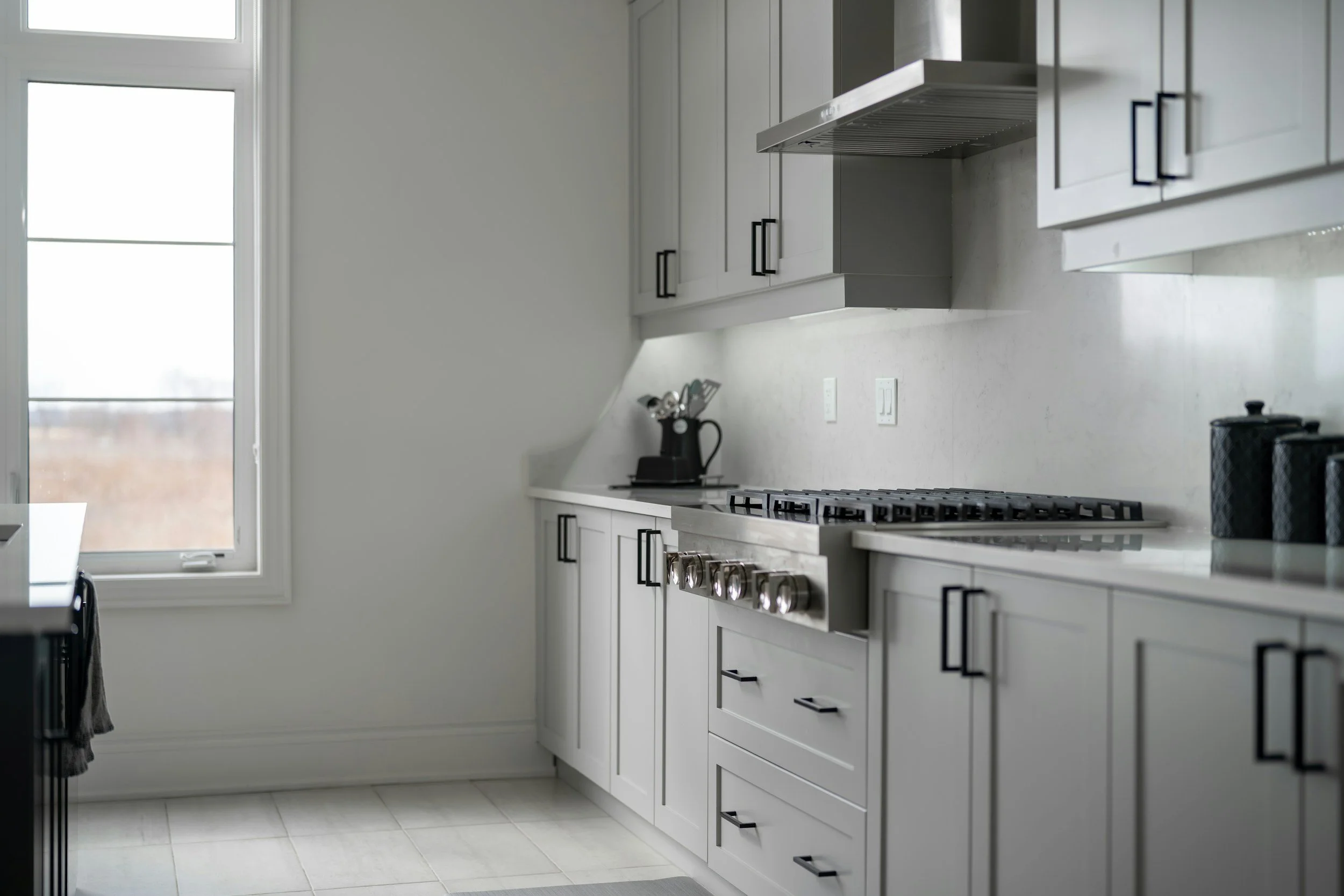 Modern kitchen with white cabinets, a stainless steel oven and stove, black handles, and a large window letting in natural light.