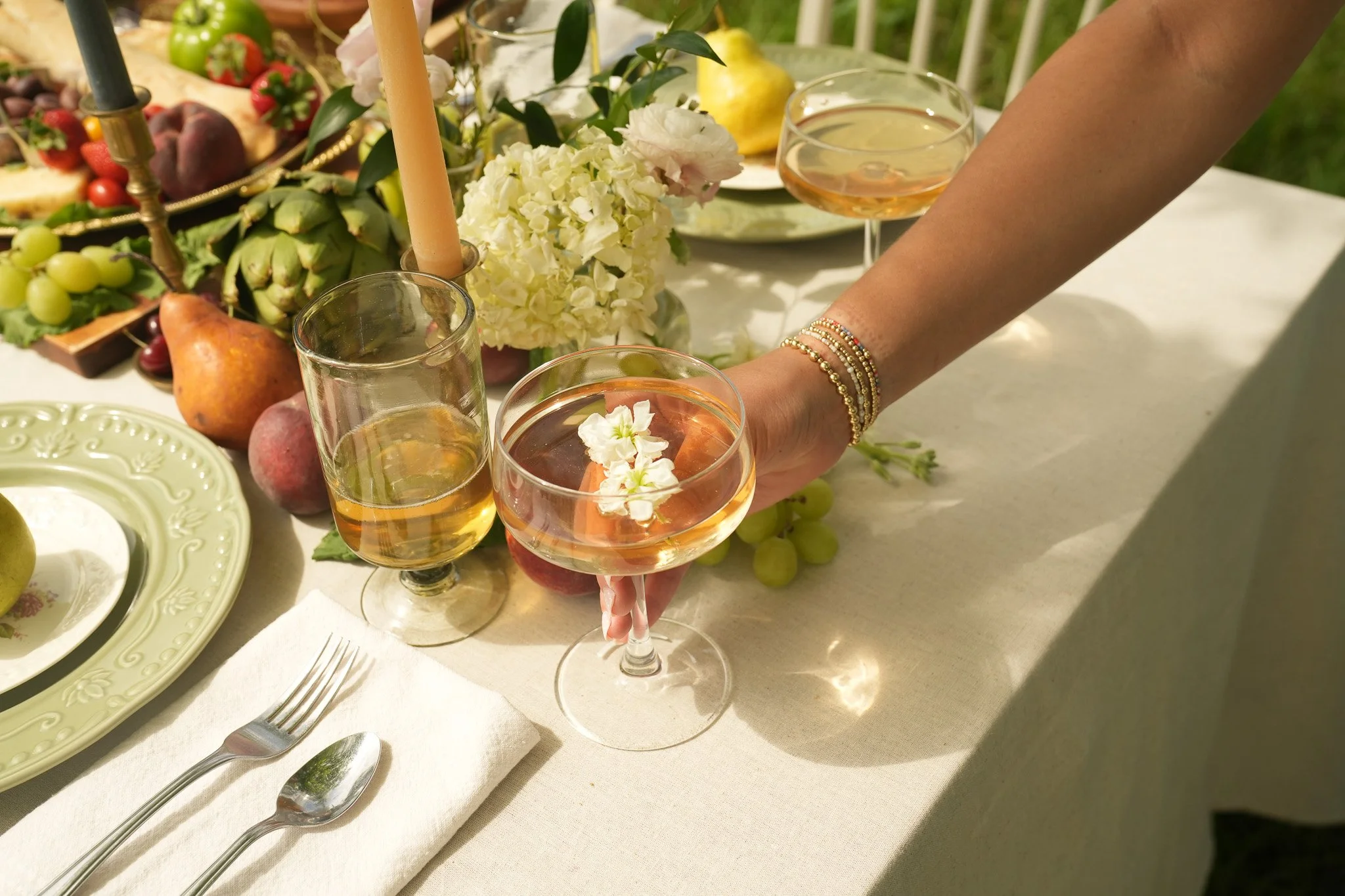 A dinner table with wine glasses, floral arrangements, and various fruits including grapes, apples, and strawberries.