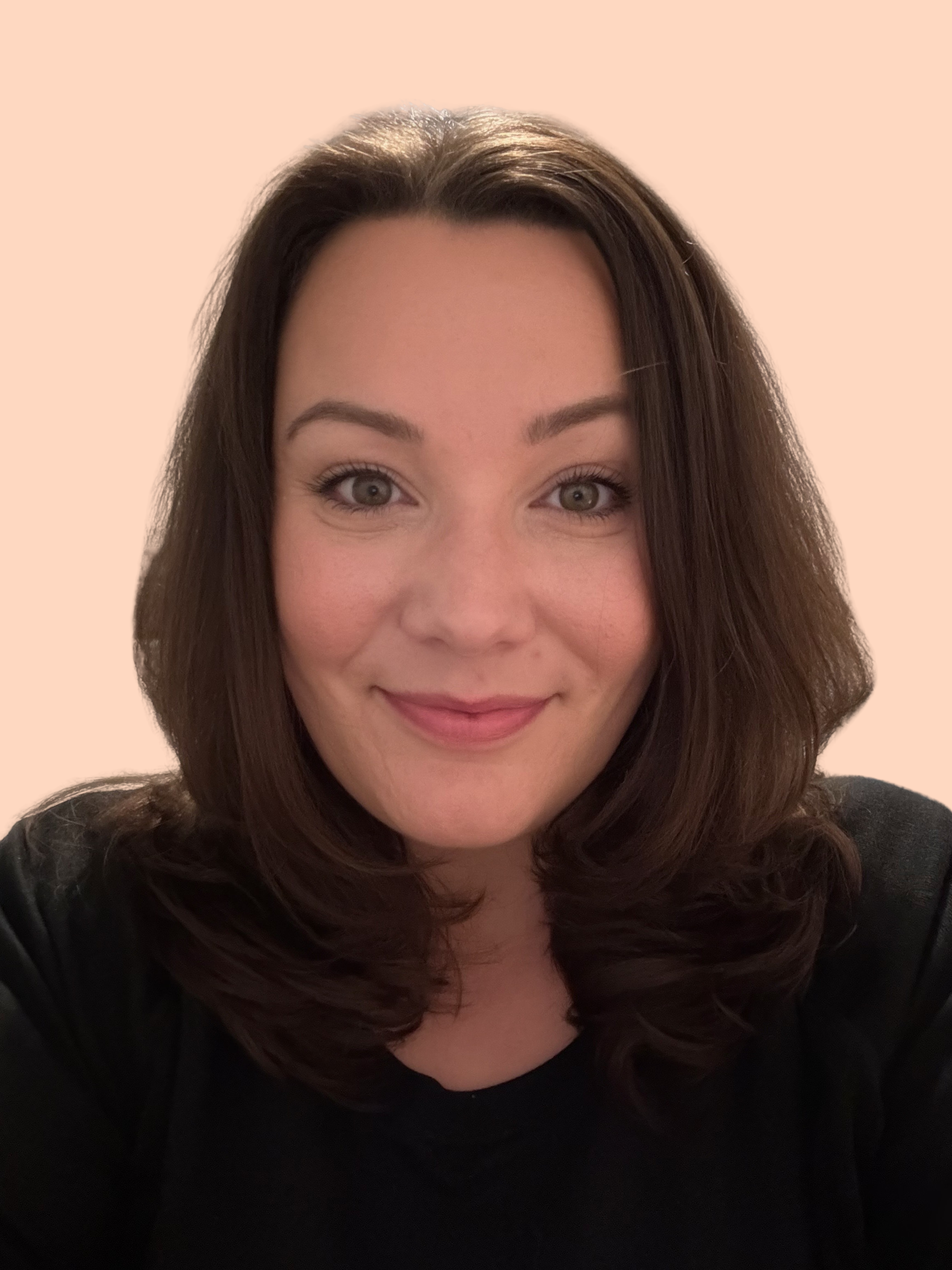 A woman with shoulder-length brown hair and gray eyes smiling at the camera, wearing a black top, with a beige background.