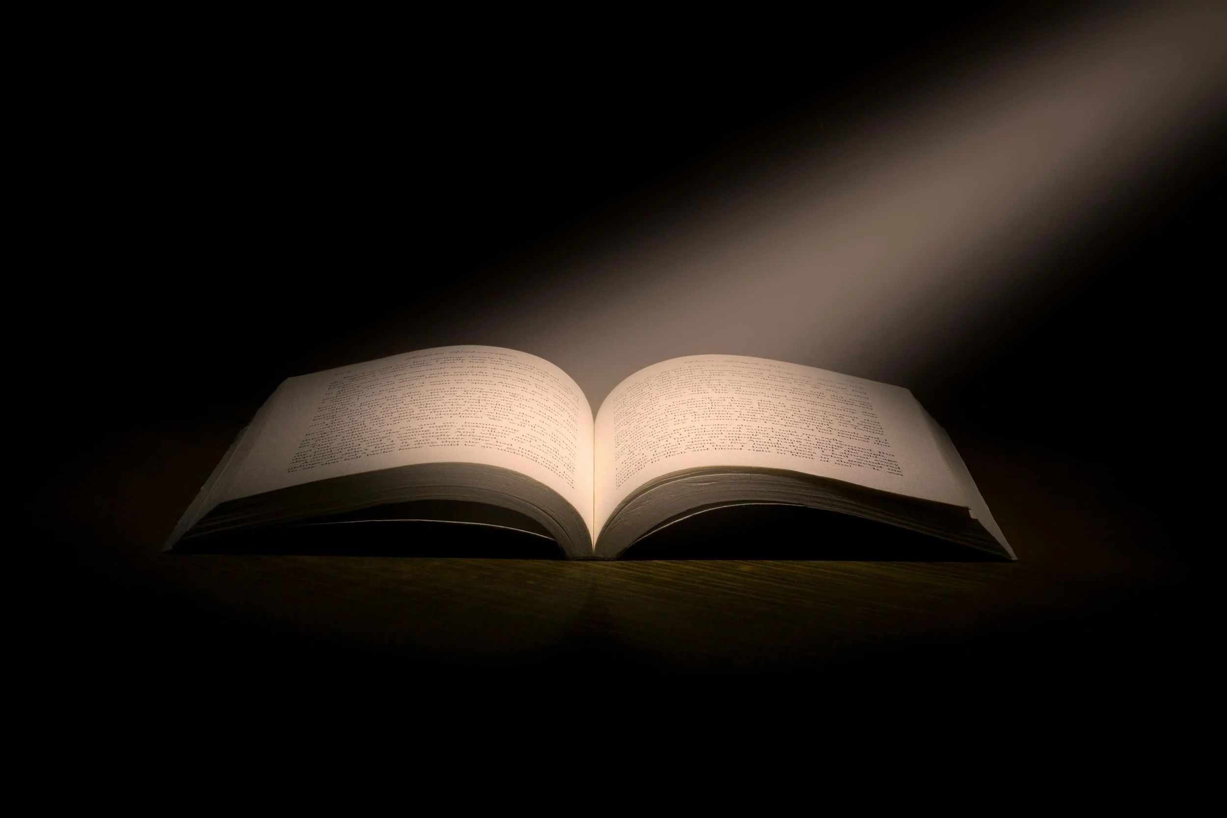Open book on a wooden surface illuminated by a focused light in darkness