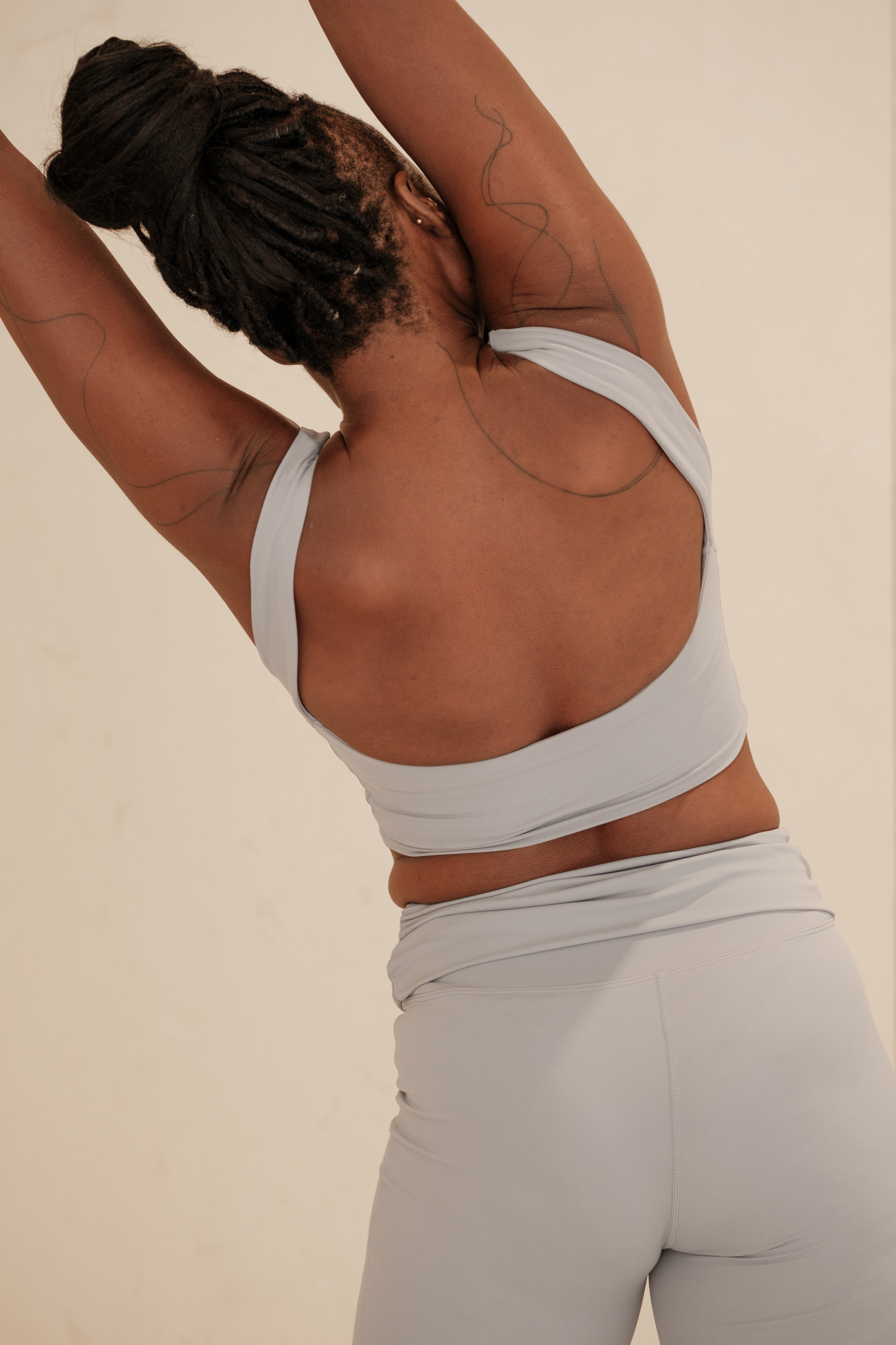 Tattooed woman stretching in front of a plain background