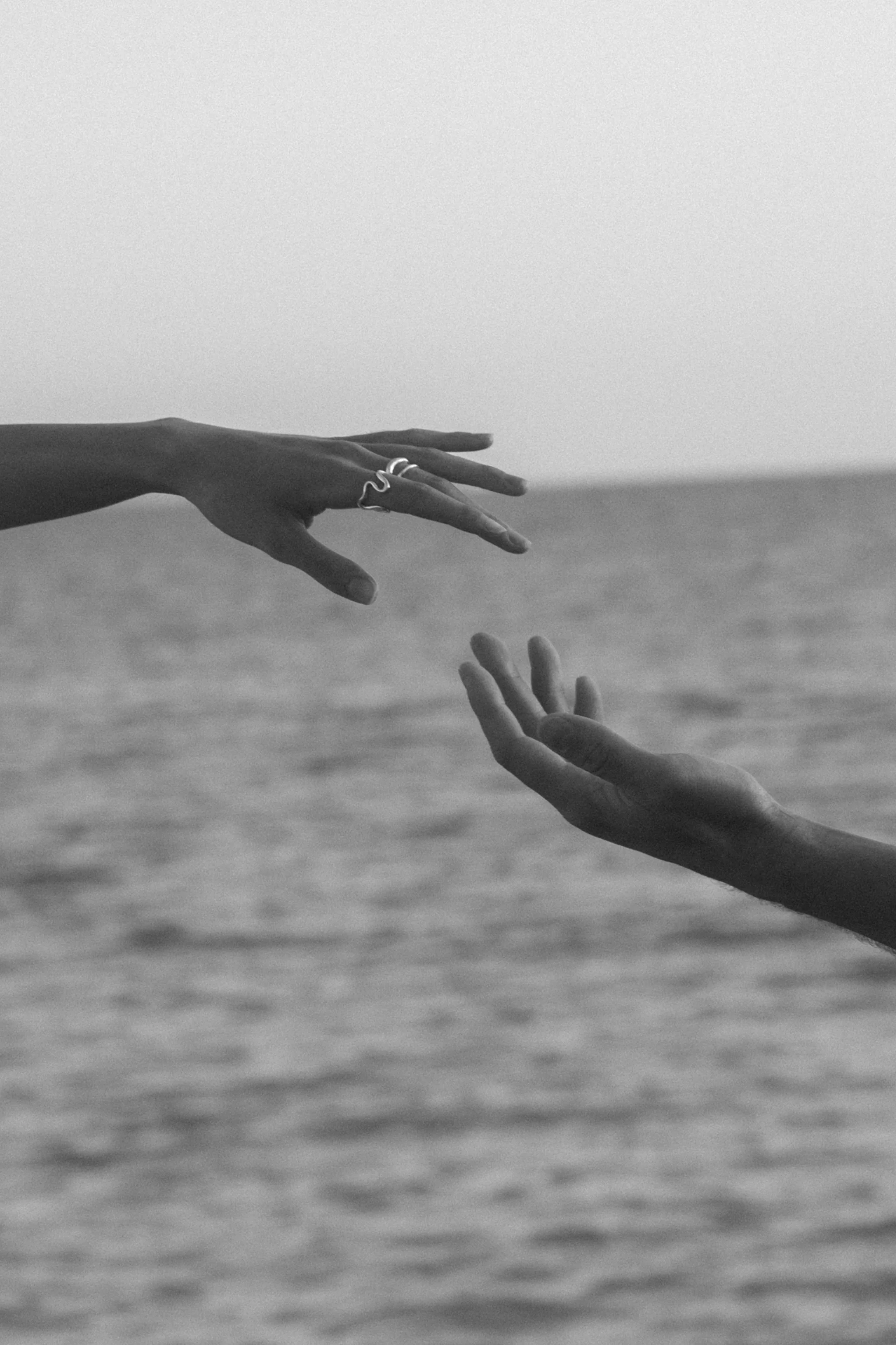 Two hands reaching out towards each other over a body of water, symbolizing connection or help, in black and white.