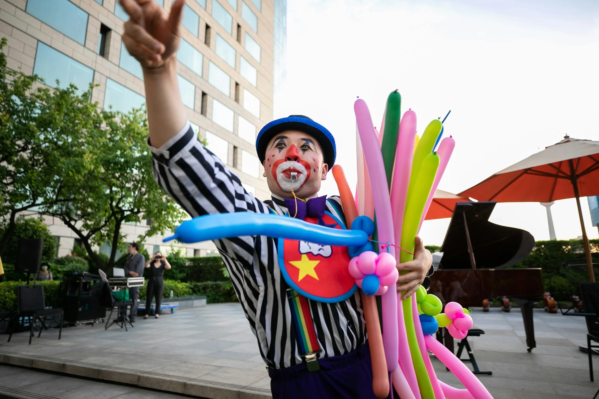 A photo of a clown dressed in a black and white shirt passing out balloons on the street
