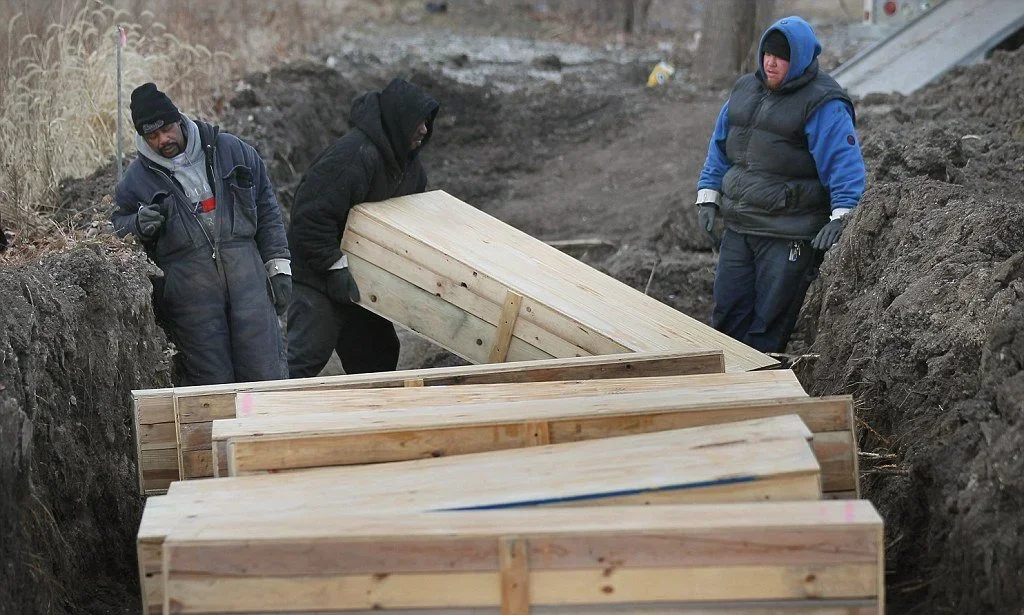 A photograph of two men loading a wooden coffin to the grround as part of a pauper's burial