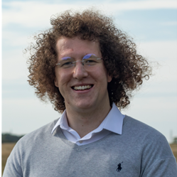 Steffan Wilkinson, Wellcare Health, Beverley with curly hair and glasses, wearing a light blue shirt and a gray sweater, standing outdoors with a cloudy sky in the background.