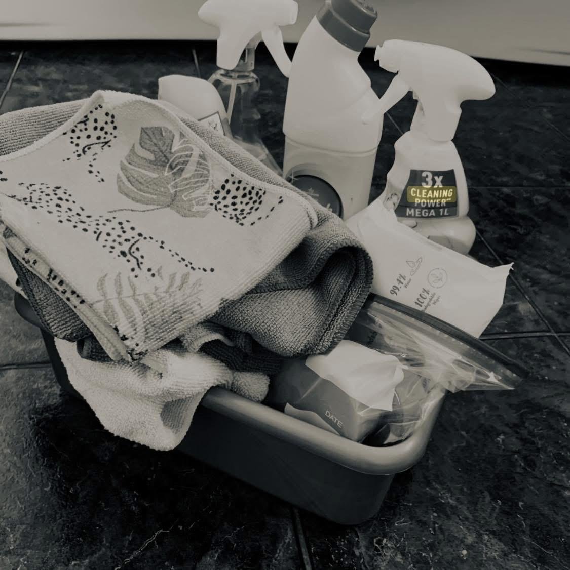 Cleaning supplies, including spray bottles, a cloth, and a cleaning sponge, arranged in a container on a tiled floor.