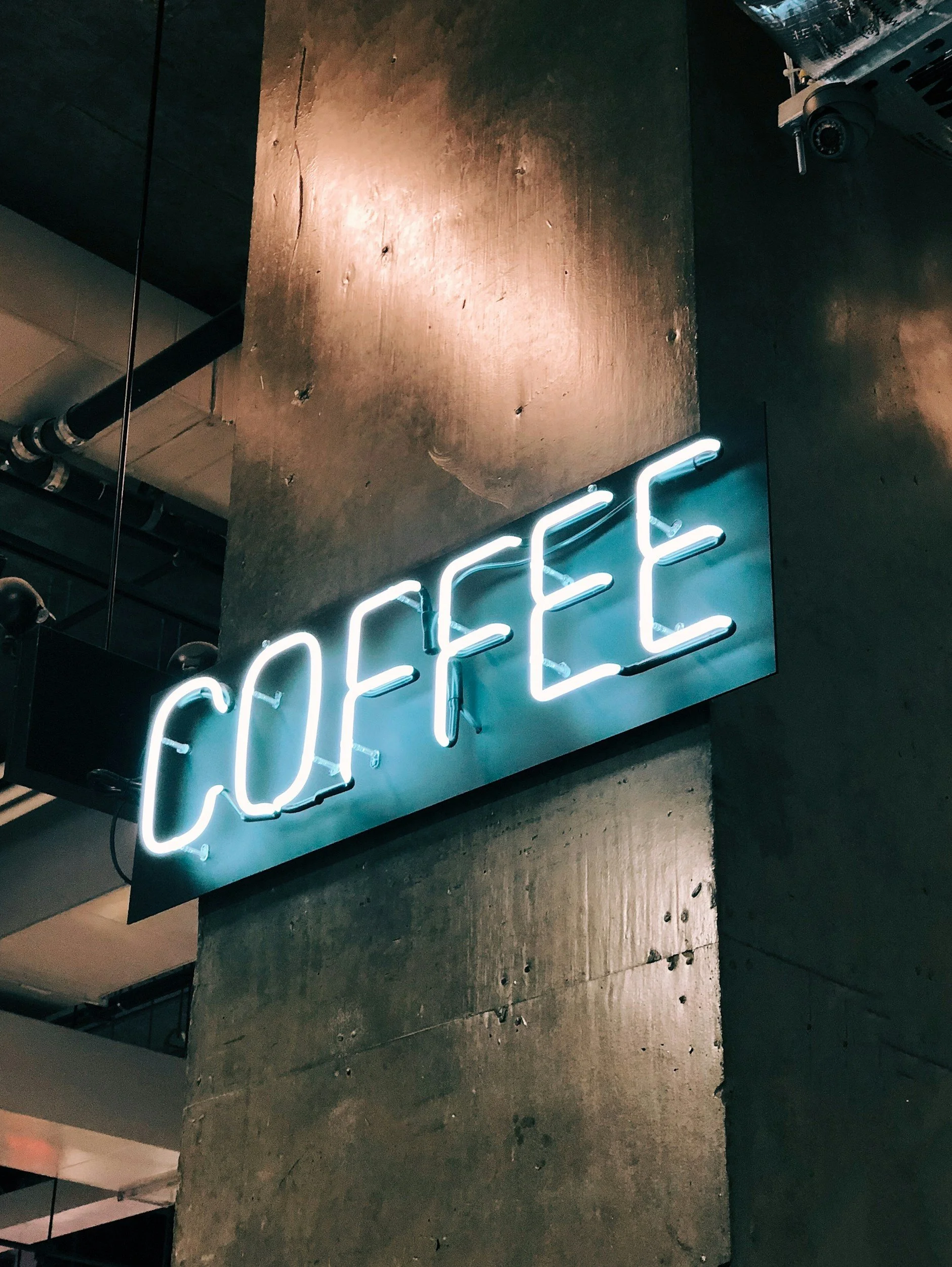Un panneau lumineux indiquant 'COFFEE' en lettres néon blanches, fixé sur un mur en béton dans un café ou un lieu public.