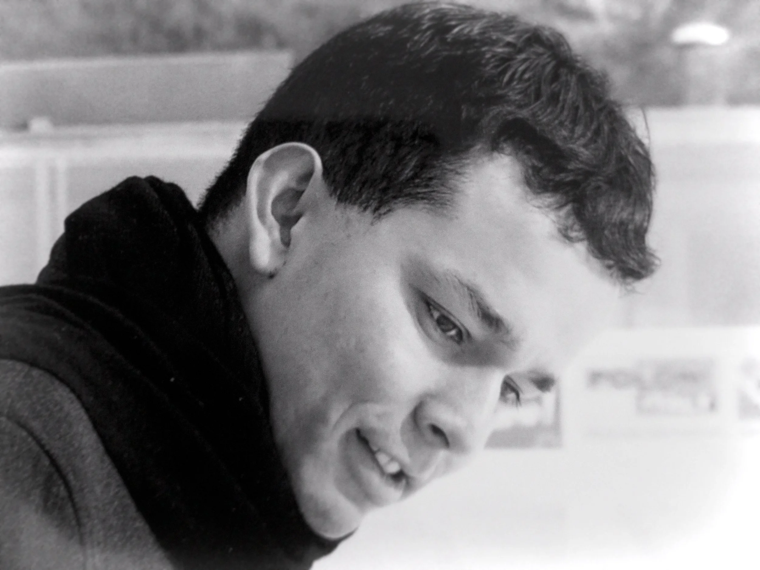 Portrait en noir et blanc d'un jeune homme regardant vers le bas avec un sourire subtle.