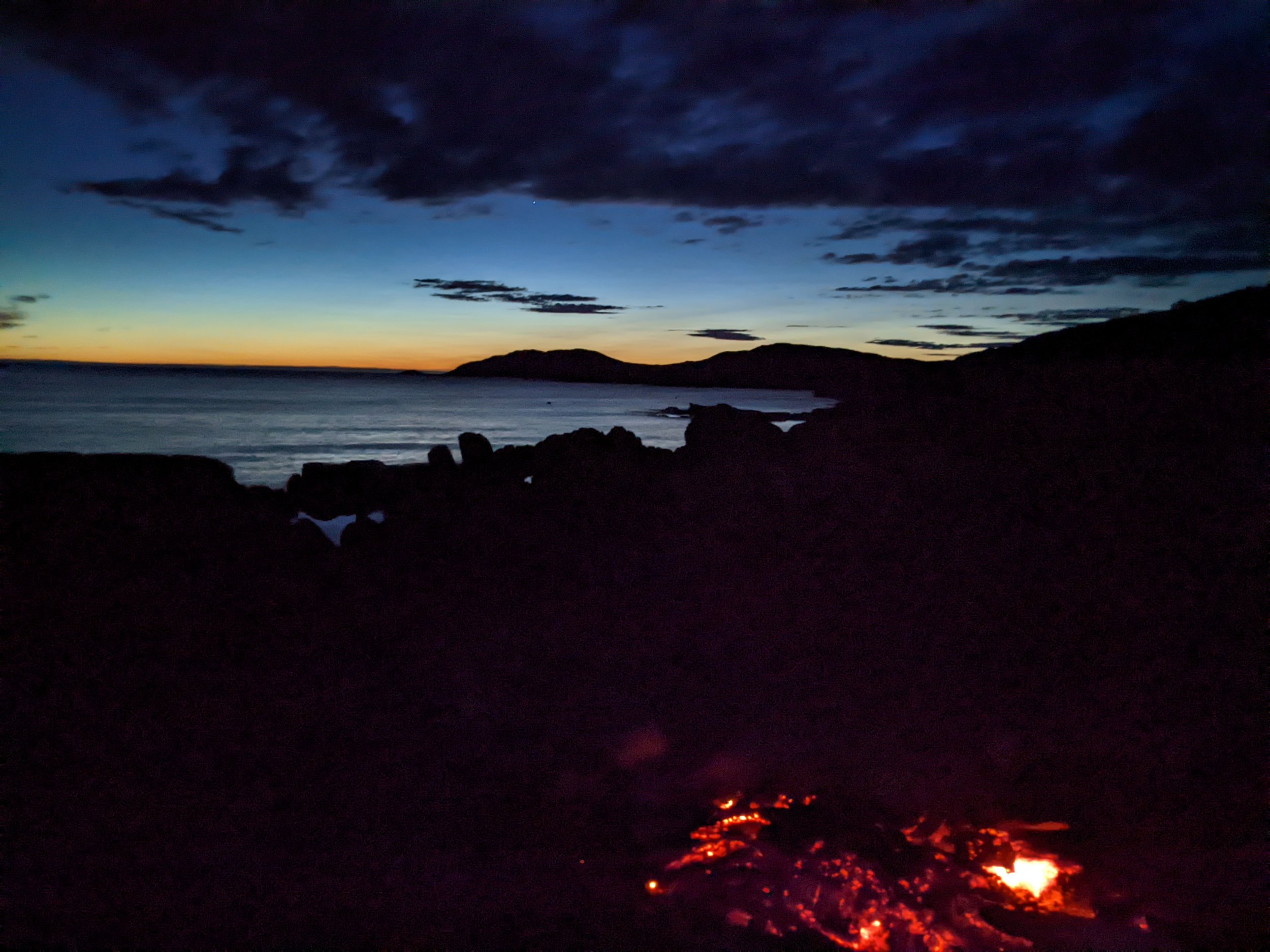 Volcanic eruption with glowing lava flowing down the dark landscape against a twilight sky with clouds.