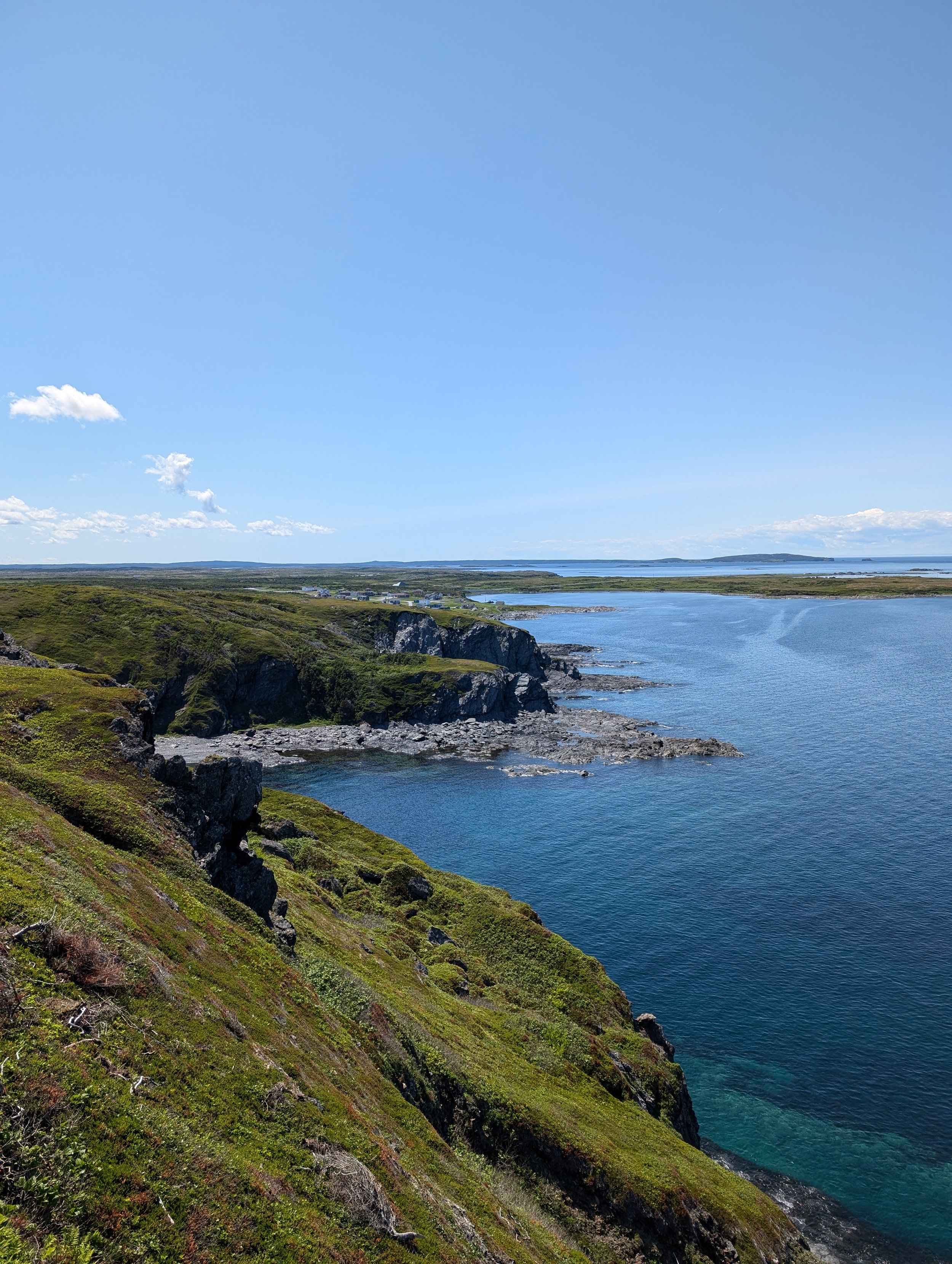 A scenic view of green cliffs along a blue body of water under a clear blue sky with some white clouds.