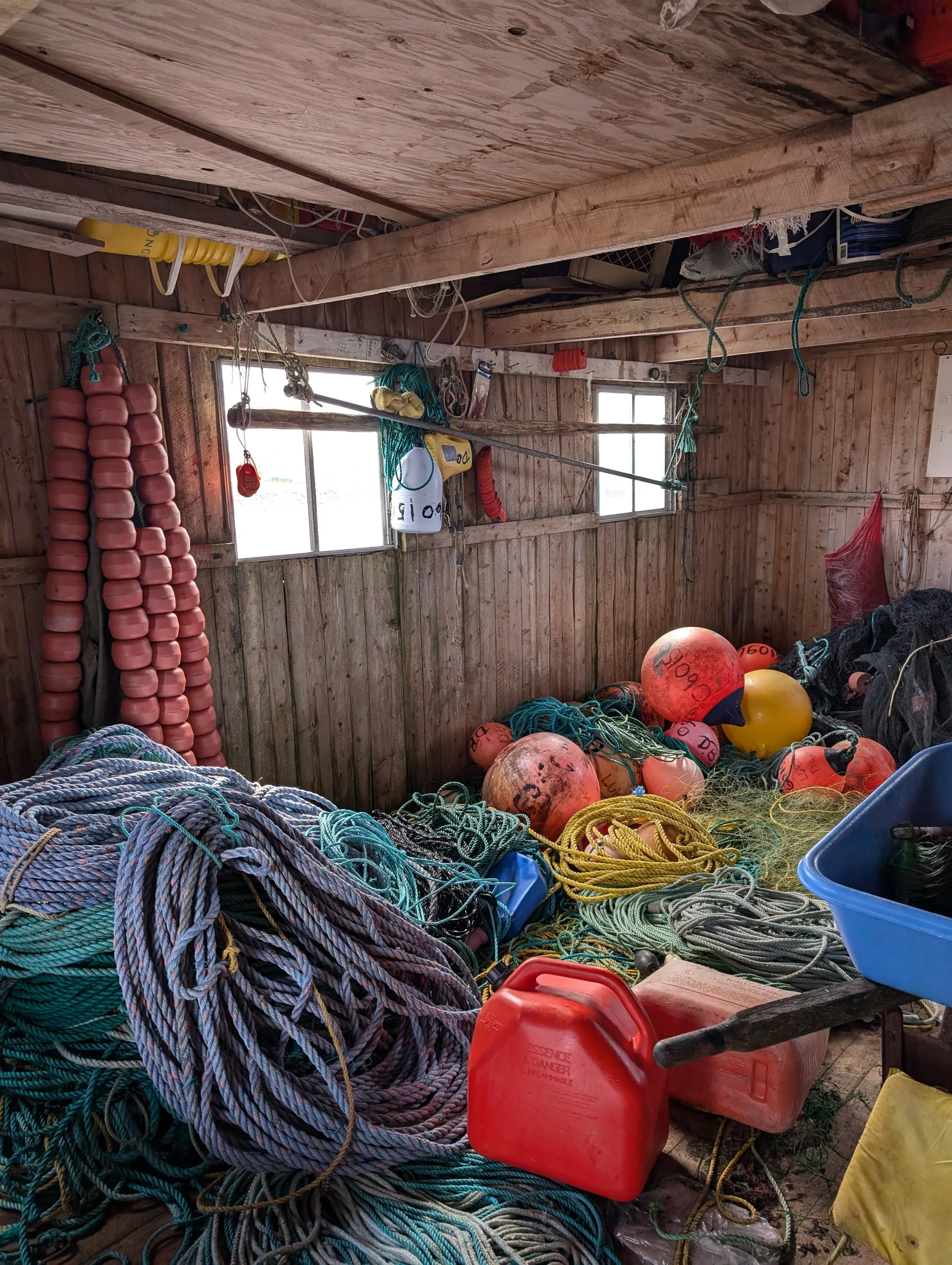 Inside a wooden shed filled with maritime equipment including ropes, buoys, and a red fuel container.